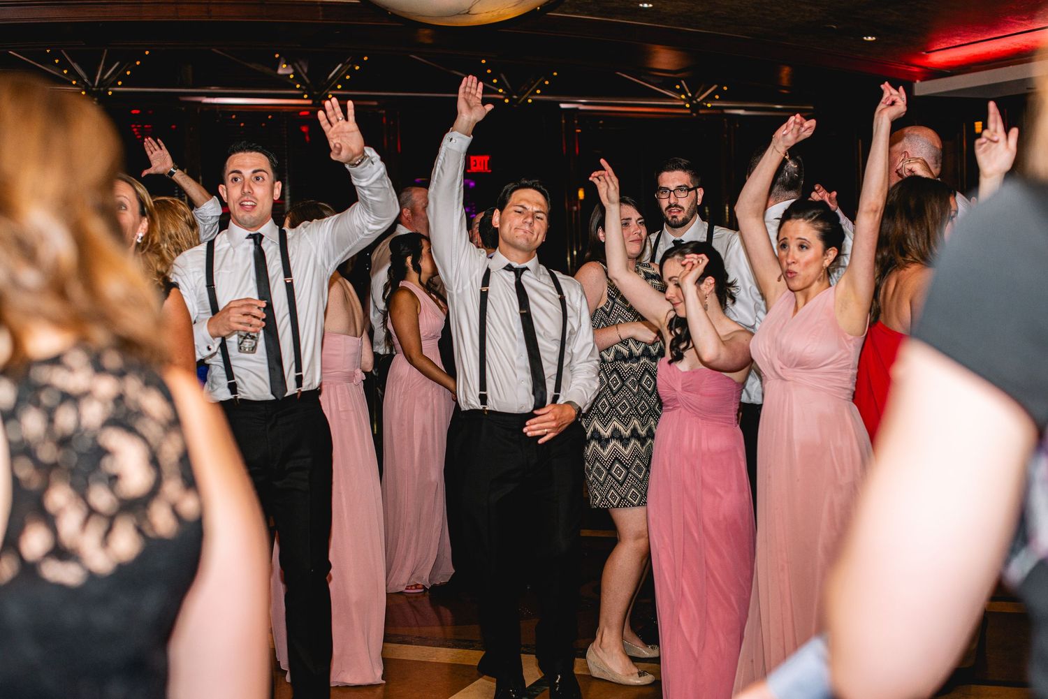 Wedding guests dancing with hands raised at a lively wedding reception party celebration.