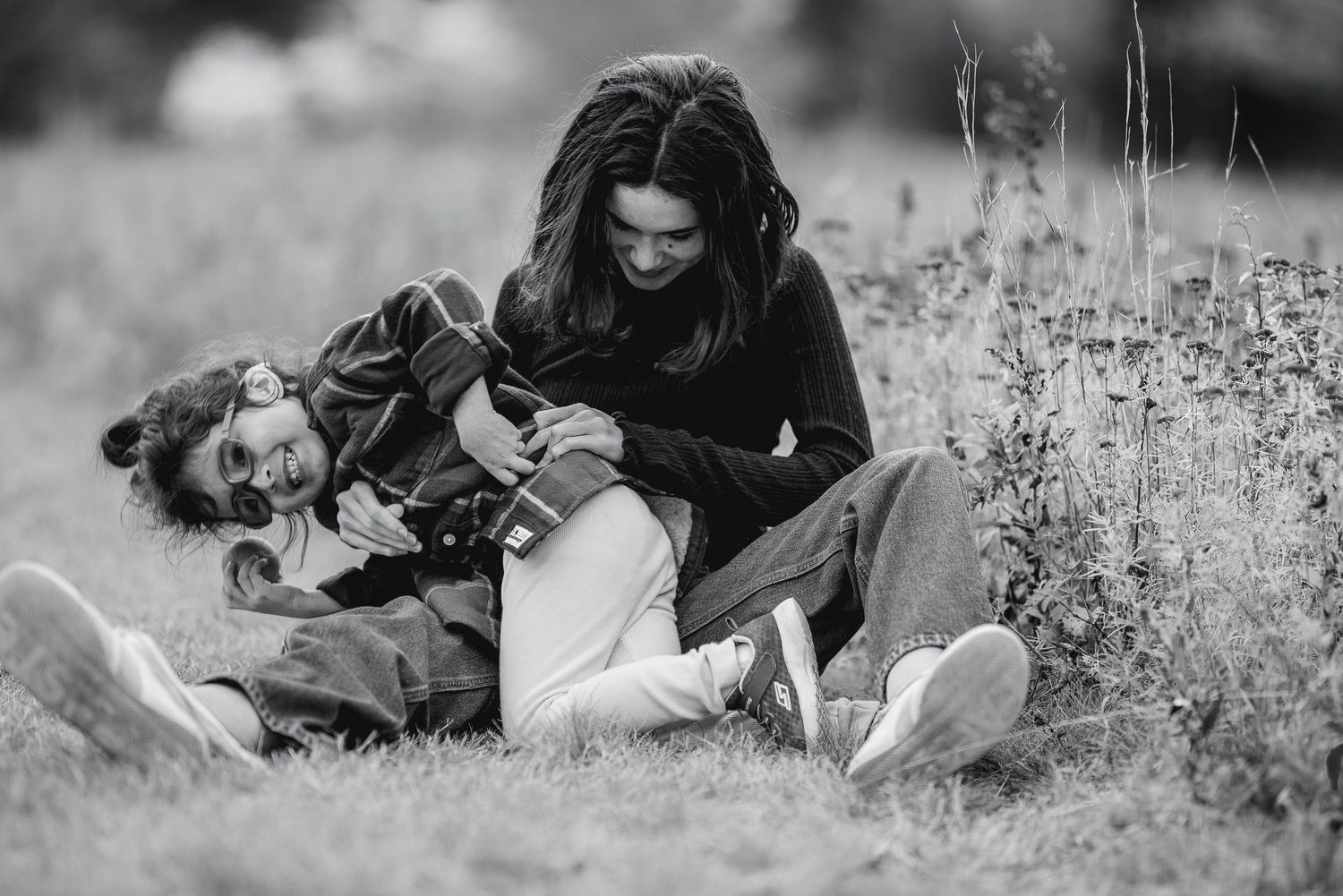 Black and white photo of a couple laughing and relaxing together in a grassy outdoor field.
