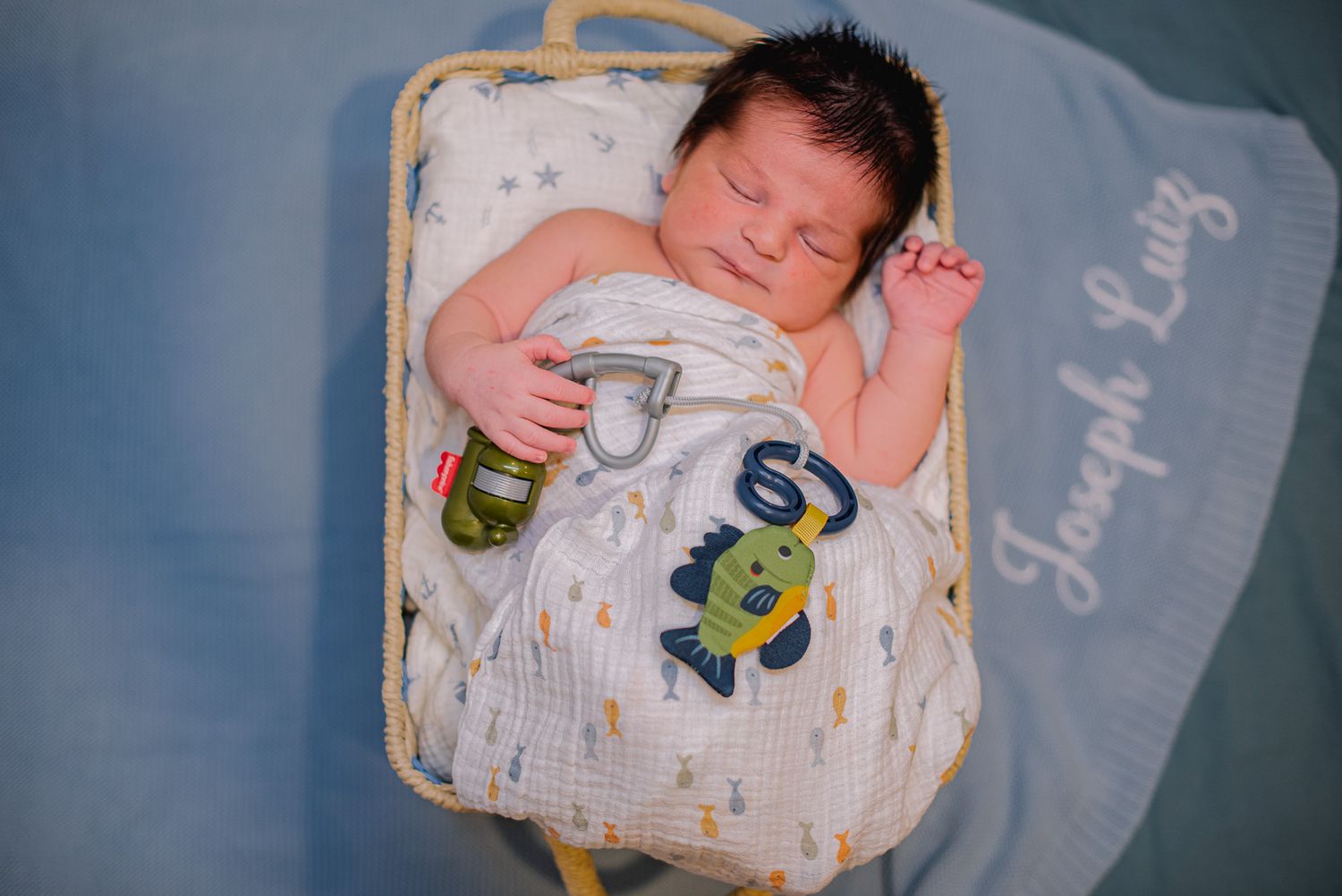 Newborn baby Joseph Luiz sleeping peacefully in a wicker basket, swaddled in a white blanket with animal prints.
