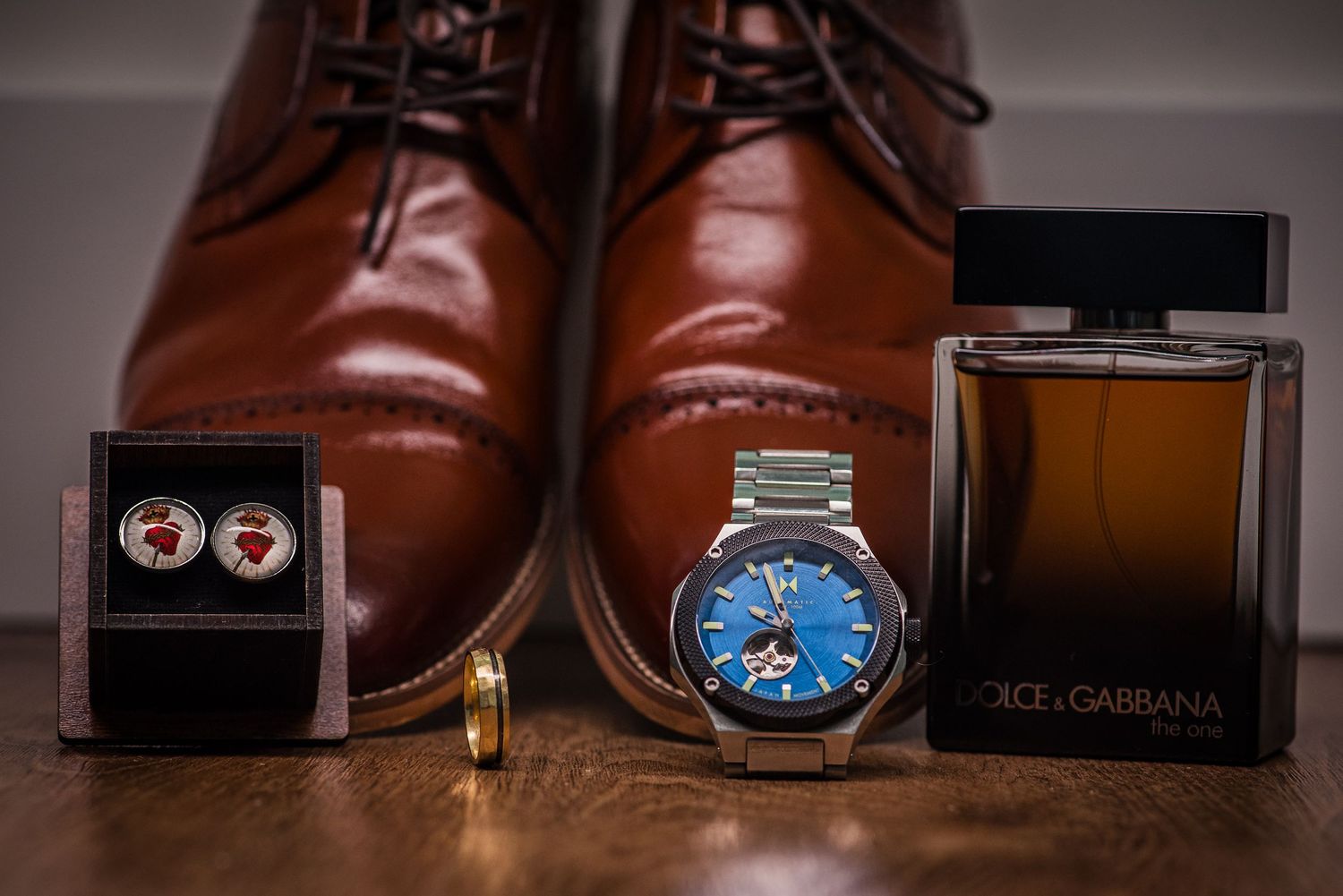 Groom accessories flat lay with brown leather shoes, blue watch, cufflinks, gold ring, and Dolce Gabbana cologne.