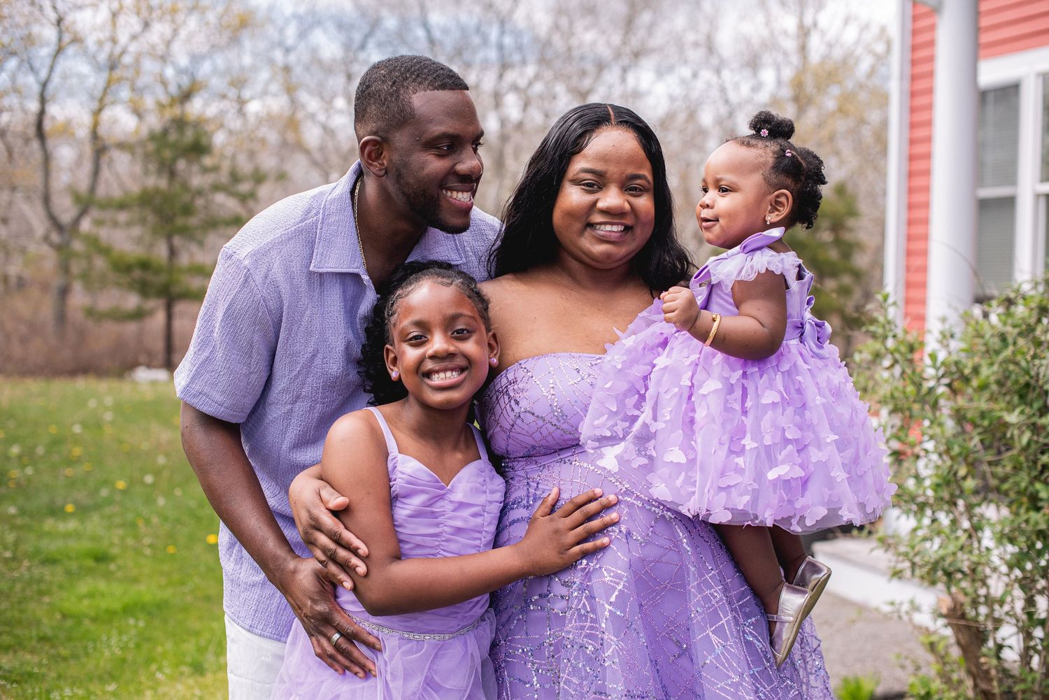Happy Black family of four in matching purple outfits smiling together outdoors in a garden setting.