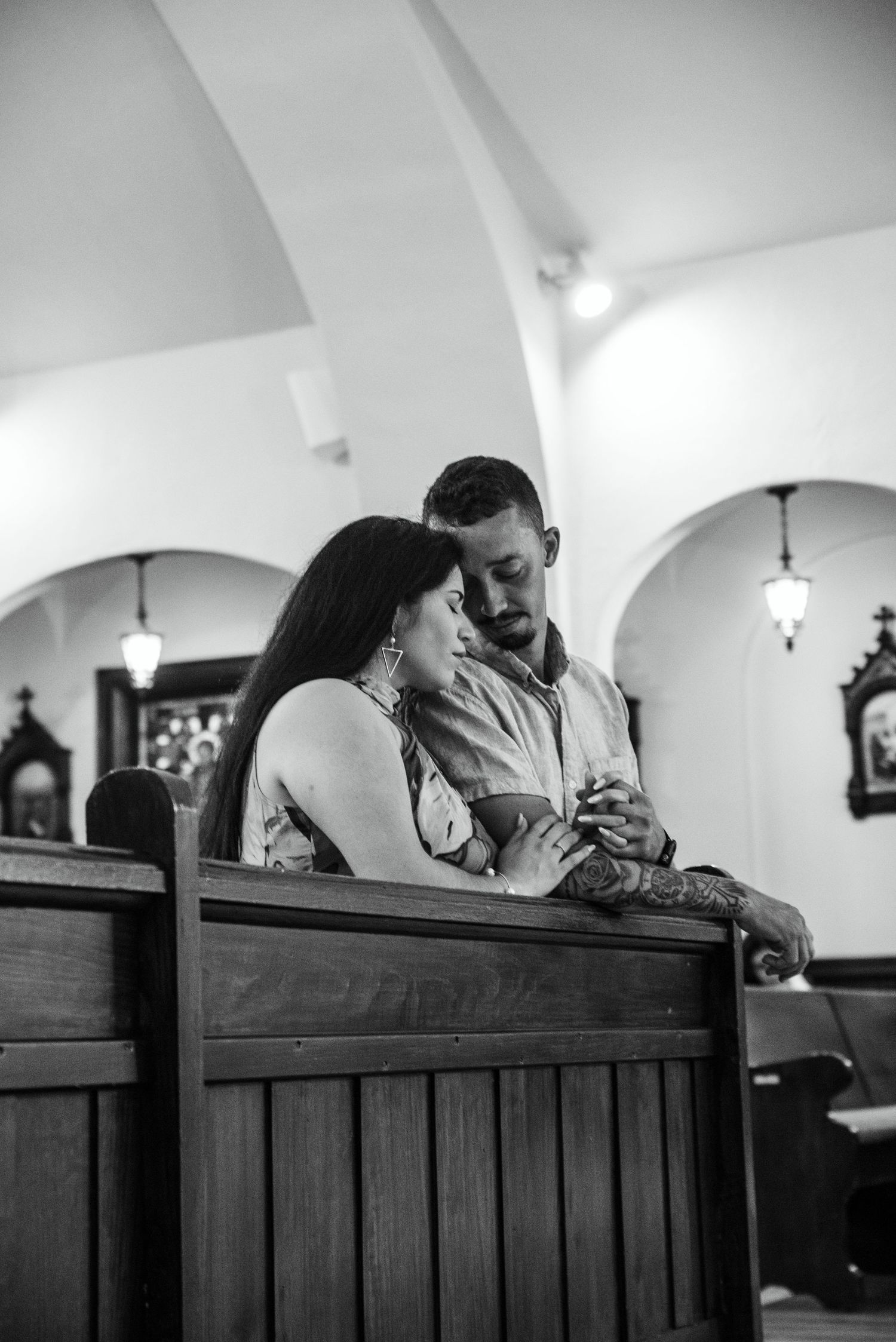 Black and white photo of couple sharing intimate moment in church pew.