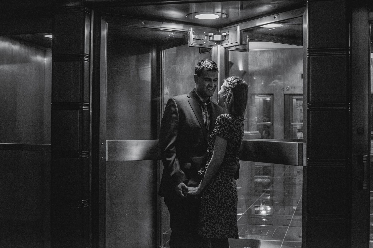 Black and white photo of a couple sharing an intimate moment inside an elevator.