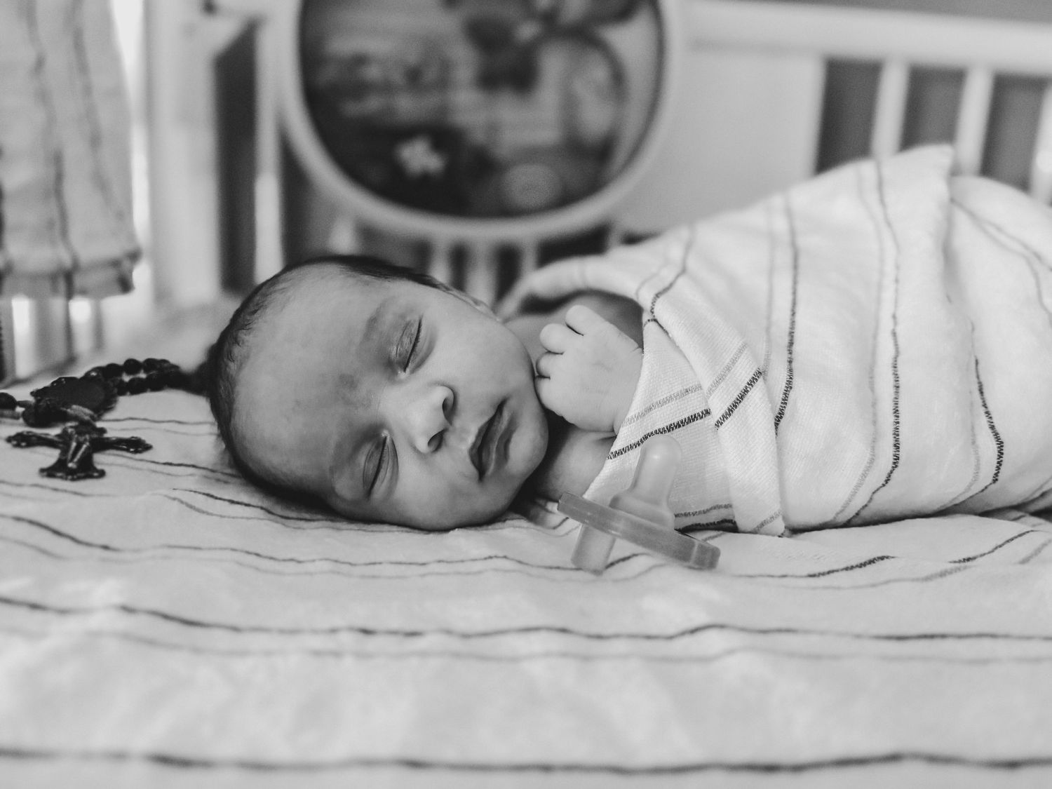 Black and white photo of a sleeping newborn baby swaddled in a striped blanket, resting peacefully in a crib.