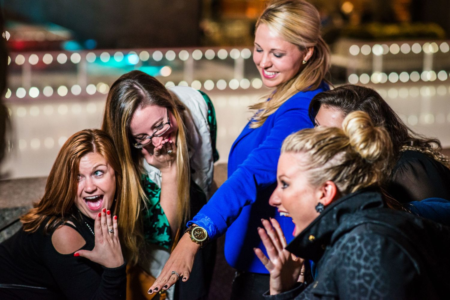 Group of excited women laughing and reacting with surprise at a nighttime outdoor event.
