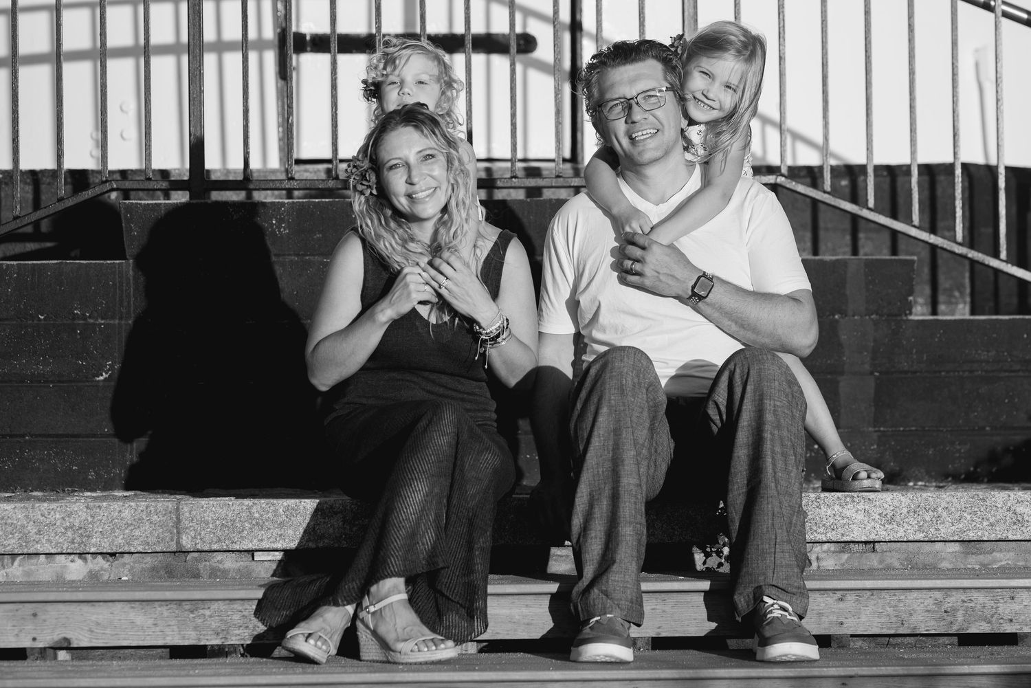Black and white photo of a happy family of four sitting on outdoor steps, smiling together.