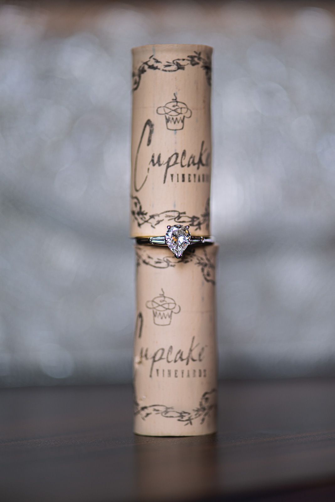 Heart-shaped diamond engagement ring displayed on a Cupcake Vineyards wine bottle tube on a wooden surface.