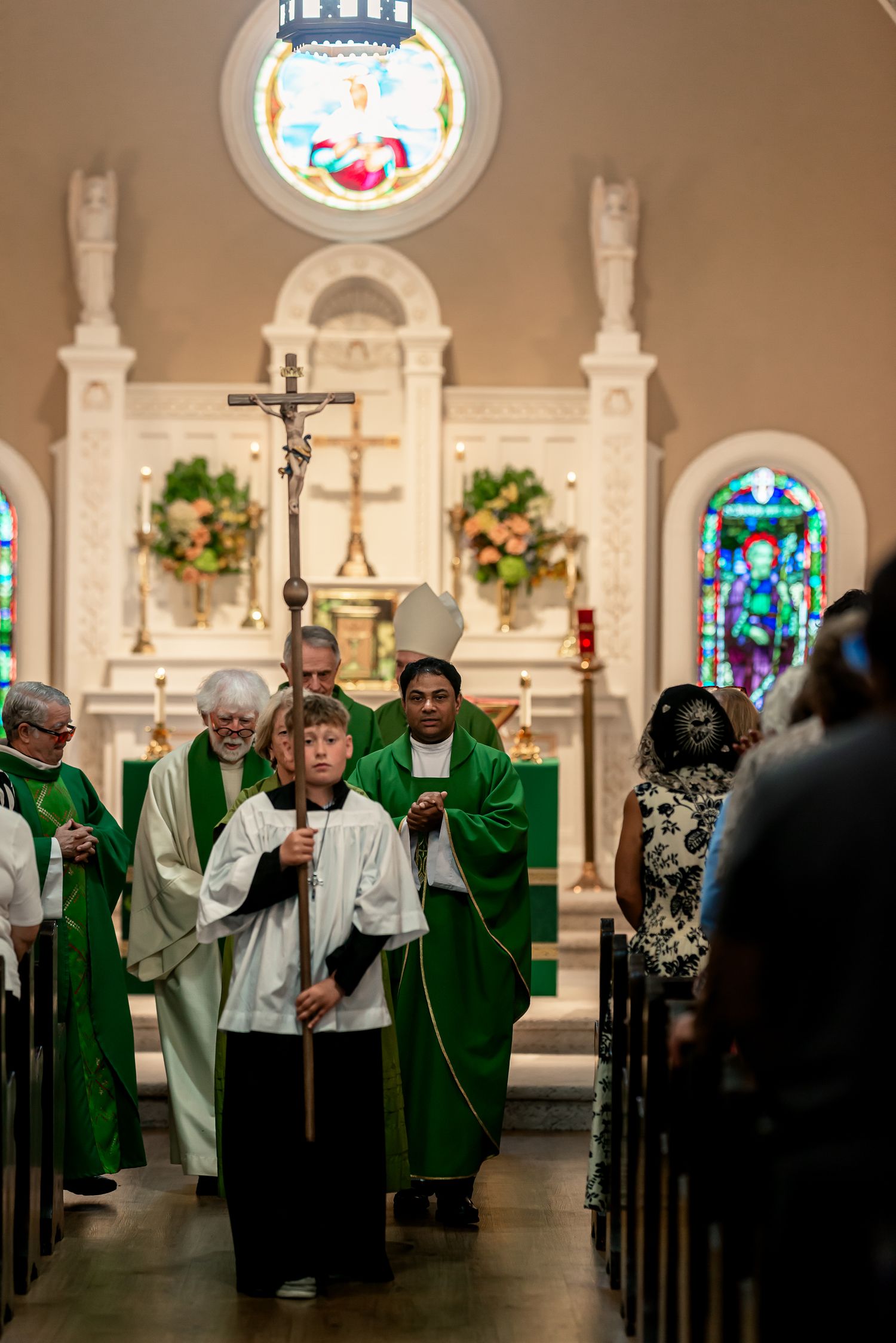 Catholic wedding recessional procession down church aisle with priests in green vestments.