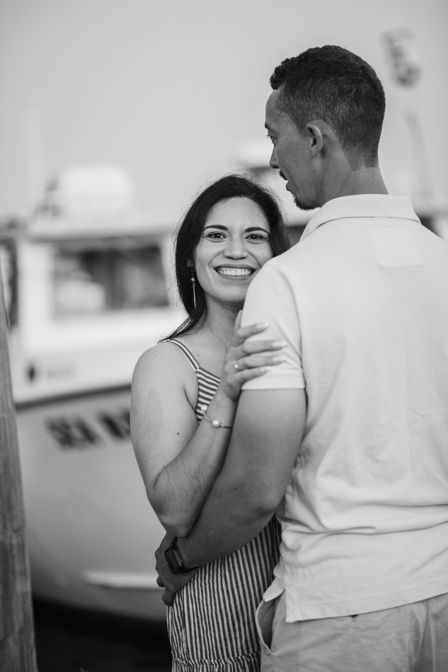 Black and white photo of smiling woman embracing man near boat at dock.