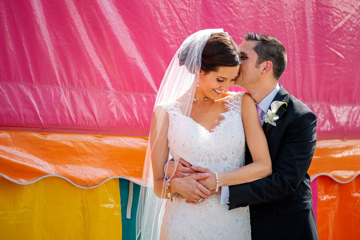 Bride and groom share a romantic moment in front of a colorful striped backdrop on their wedding day.