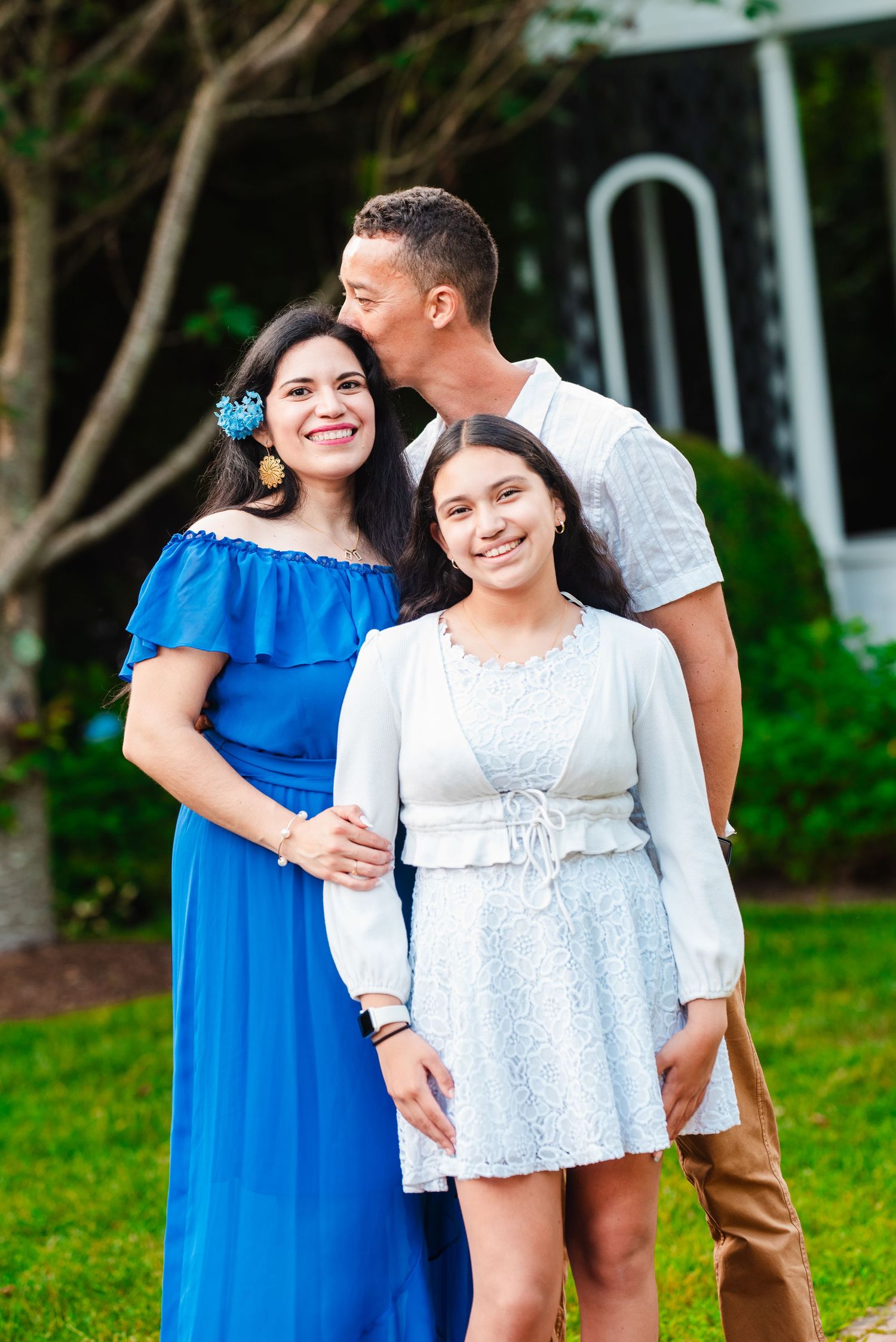 Family portrait with woman in blue dress, man kissing her cheek, teen daughter.