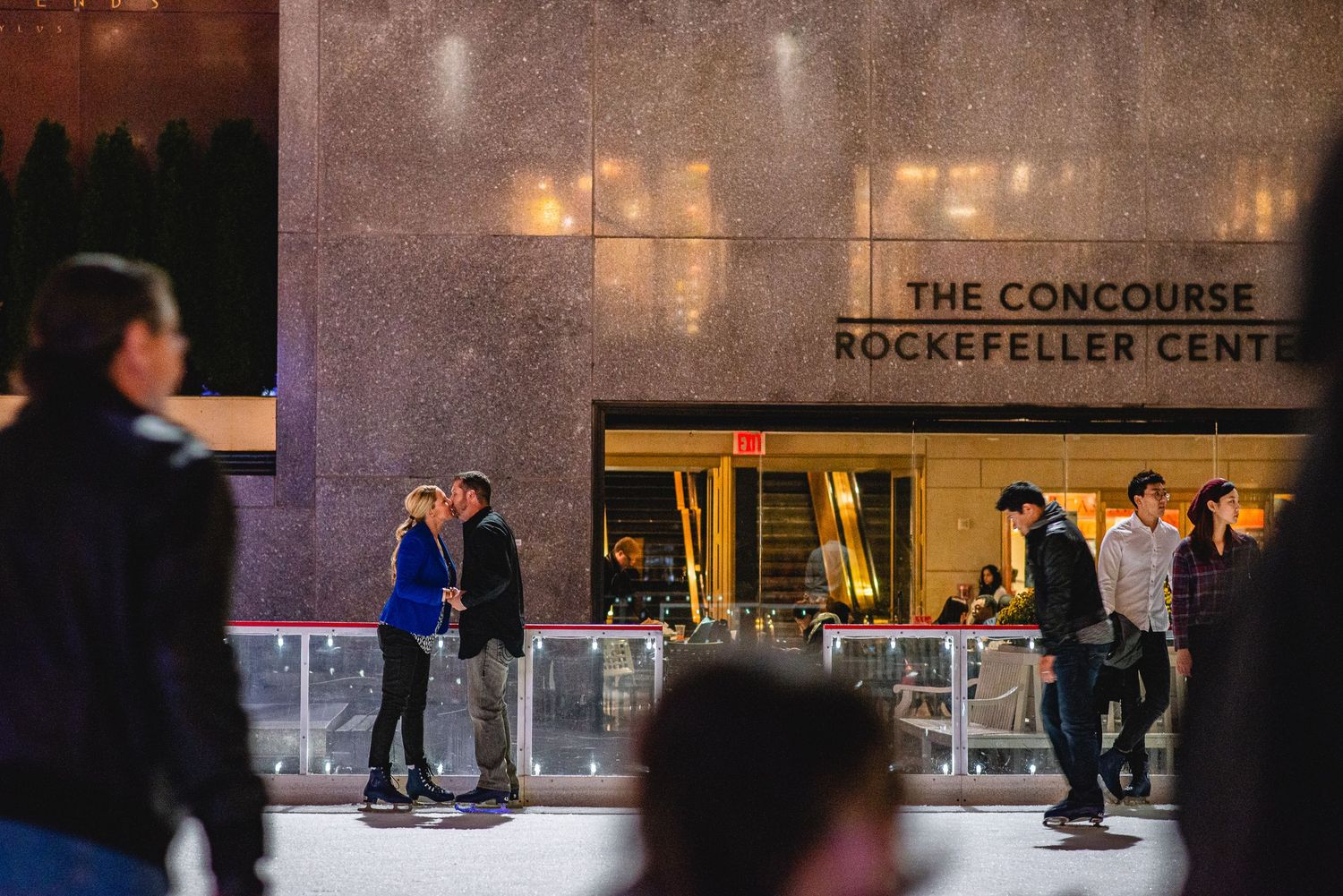 People ice skating at the Rockefeller Center Concourse rink in New York City at night.