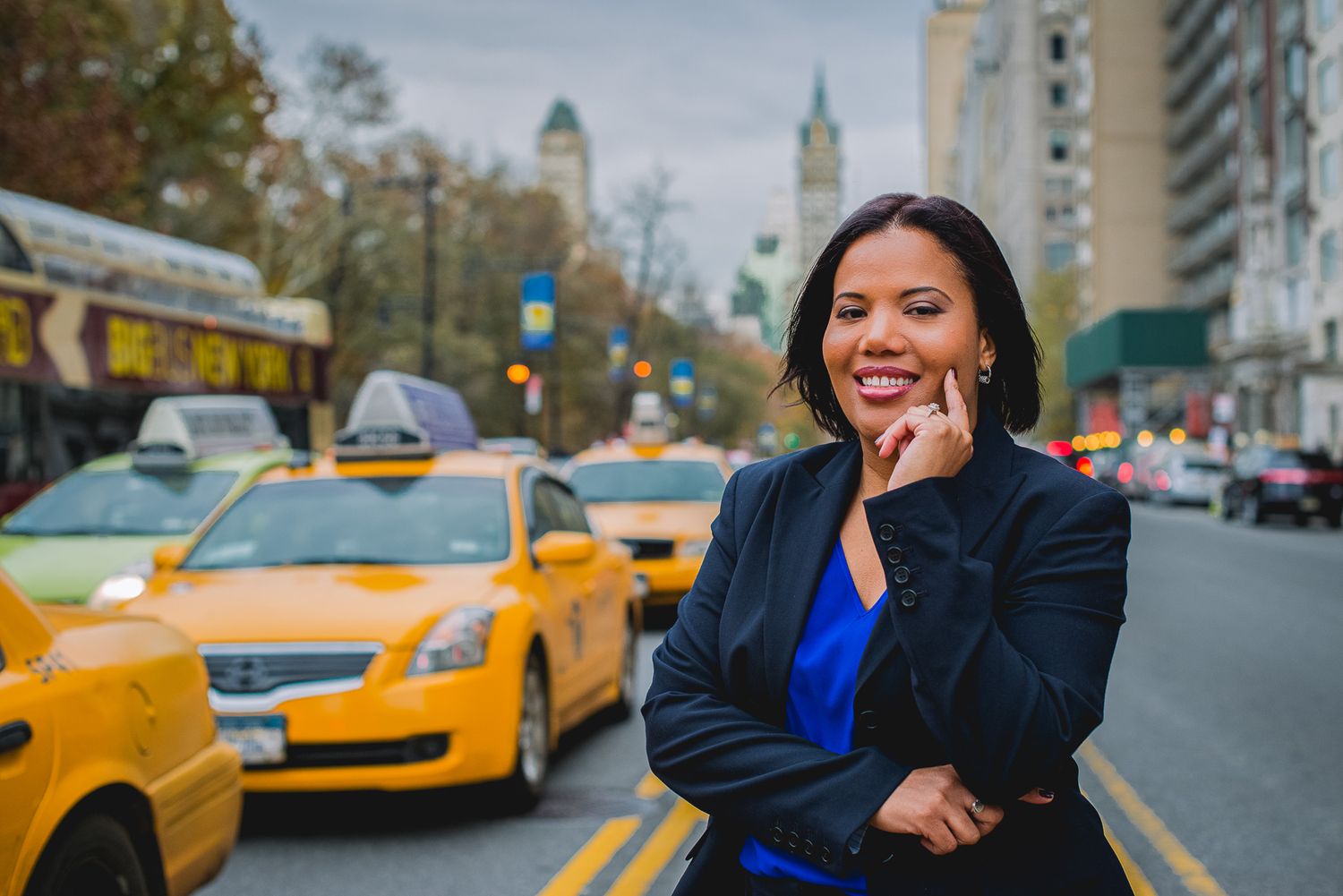 Professional woman in blue blazer smiling on NYC street with yellow taxis in background.