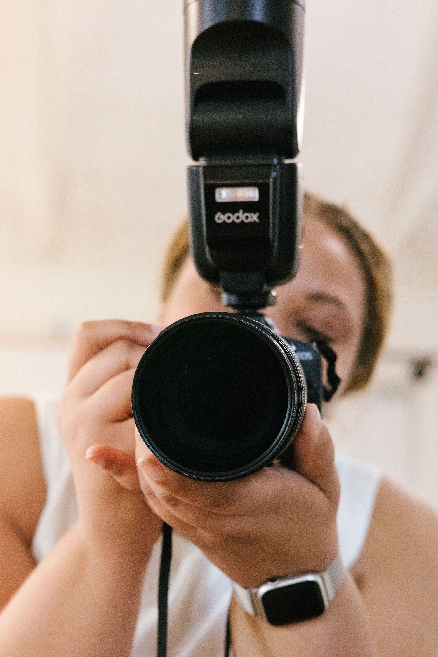Photographer holding a DSLR camera with Godox flash attachment, aiming lens directly at viewer.
