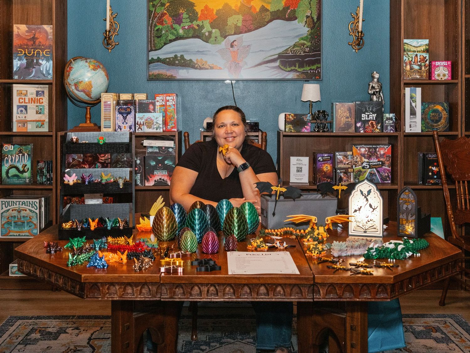 Woman smiling at ornate desk surrounded by LEGO sets, board games, and colorful collectibles in a beautifully decorated room.