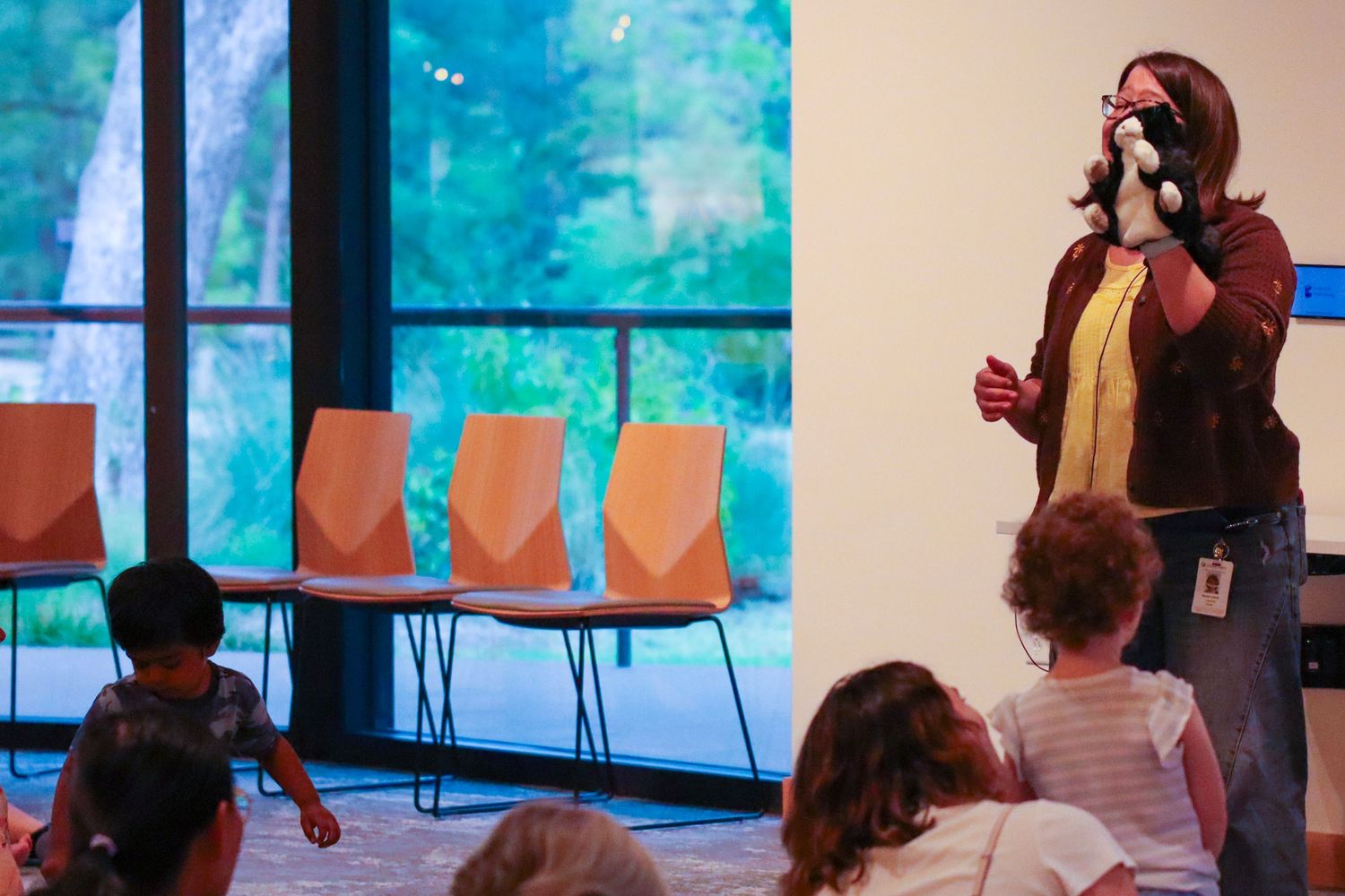 Educator uses a dog puppet to engage young children during an interactive storytime session in a modern library.
