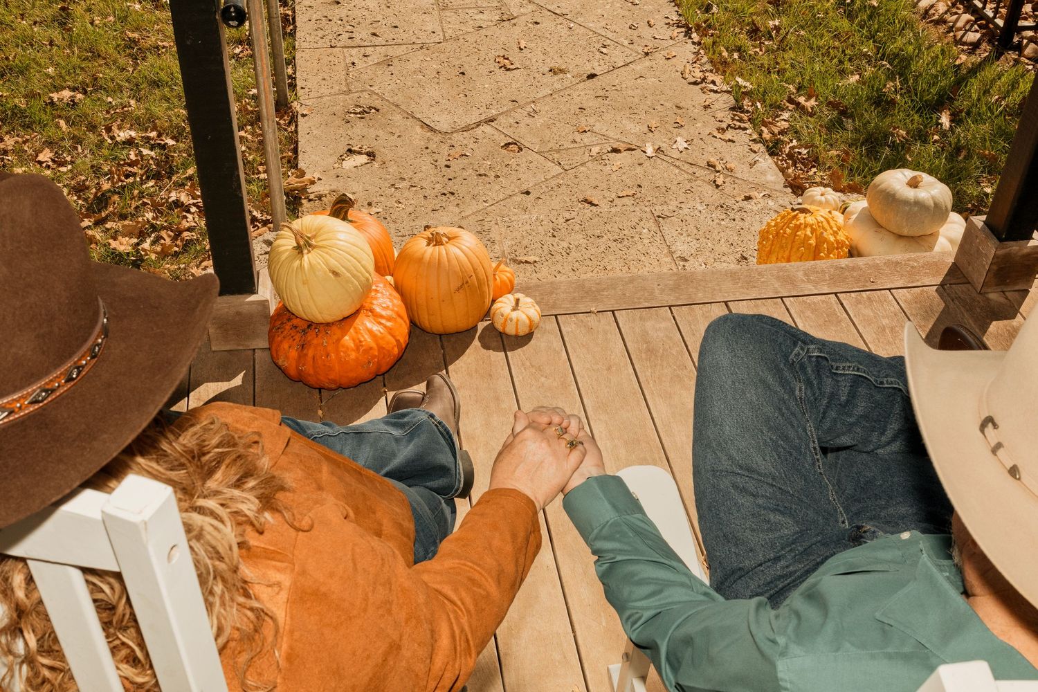 Two people relaxing on a wooden porch surrounded by colorful autumn pumpkins and gourds during fall season.