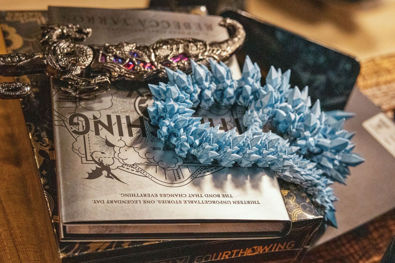 Blue crystal crown resting on fantasy books including Fourth Wing on a wooden table.