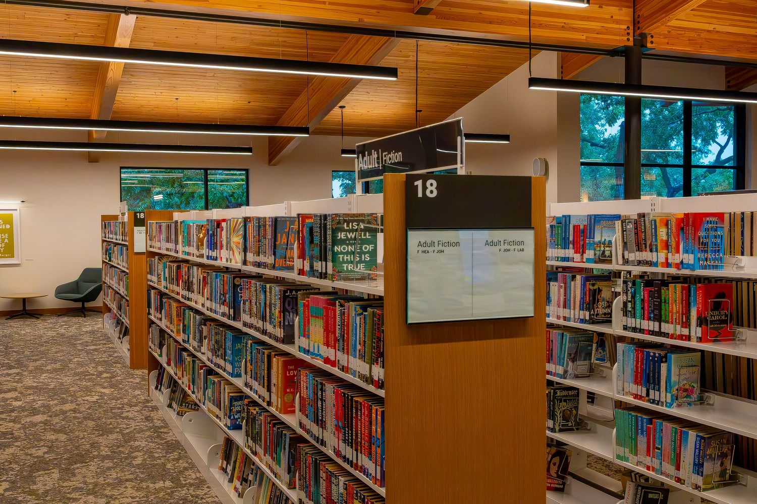 Library aisle 18 with colorful books on wooden shelves under warm ceiling lights in a modern public library.