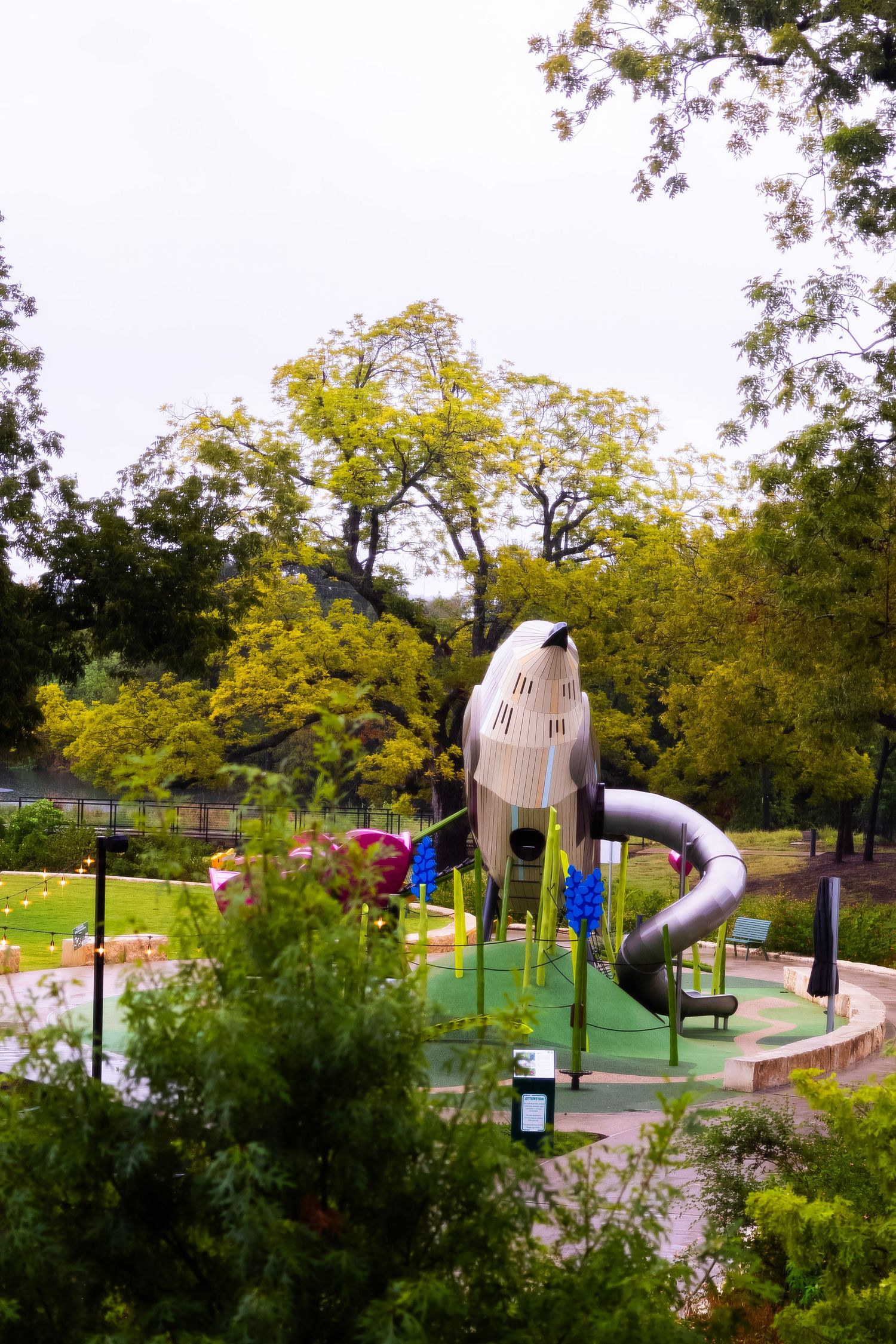 Colorful mini golf course featuring a rocket ship slide structure surrounded by lush green trees in a park setting.