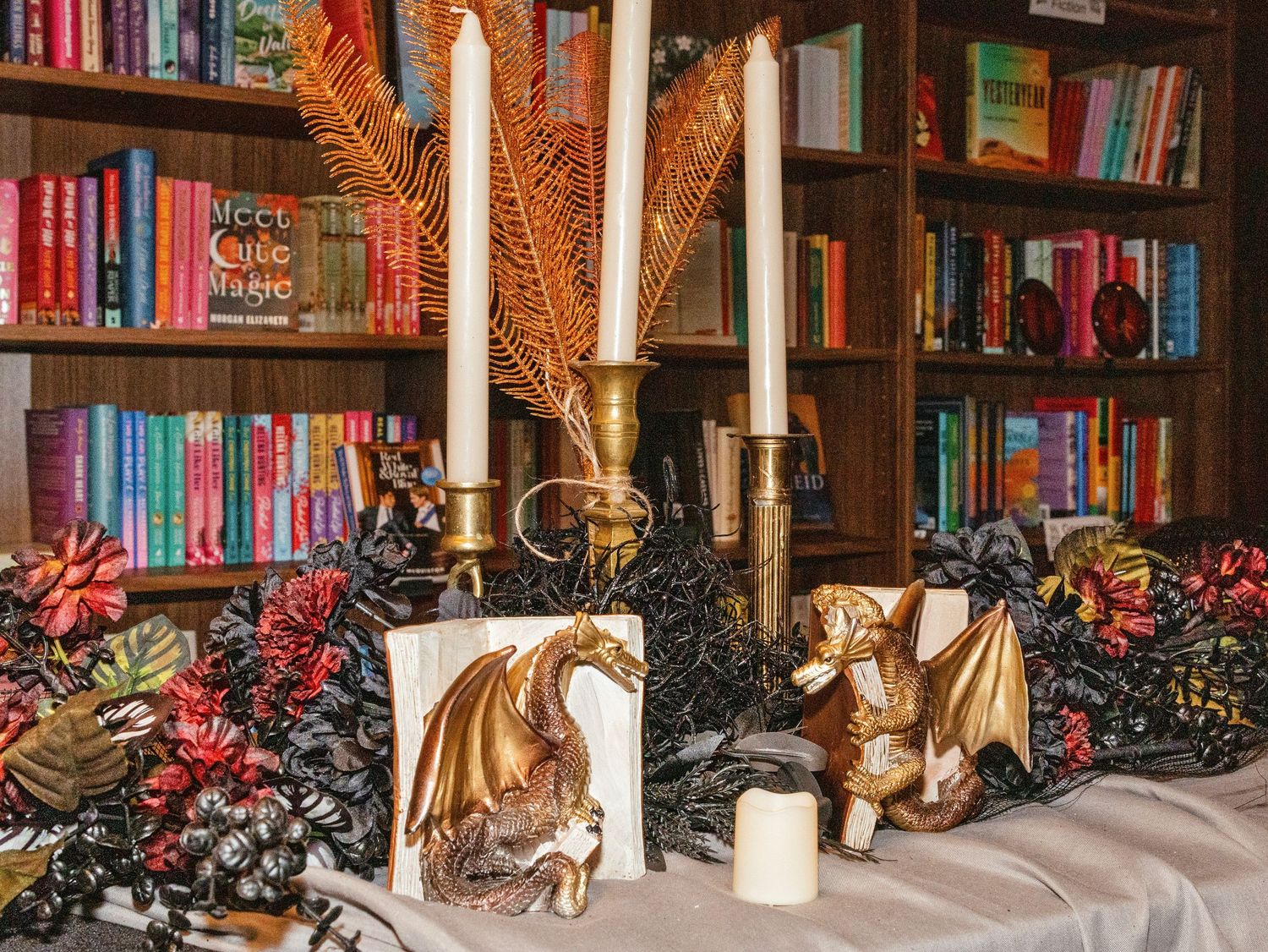 Dragon figurines and candles displayed on a table with colorful bookshelf backdrop and festive red floral decorations.