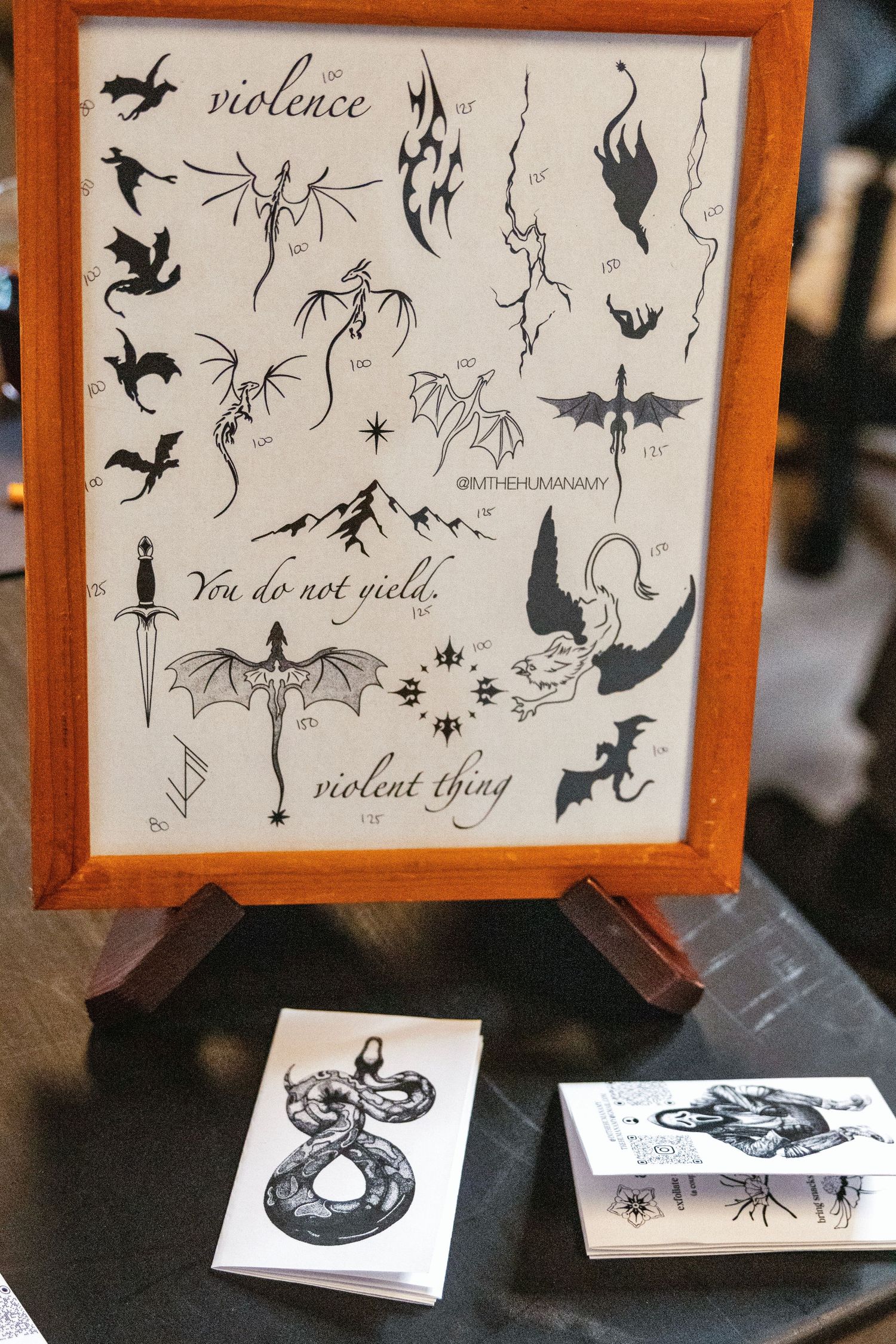 Framed flash tattoo sheet featuring dragons, daggers, and phrases like violence and violent thing on display.