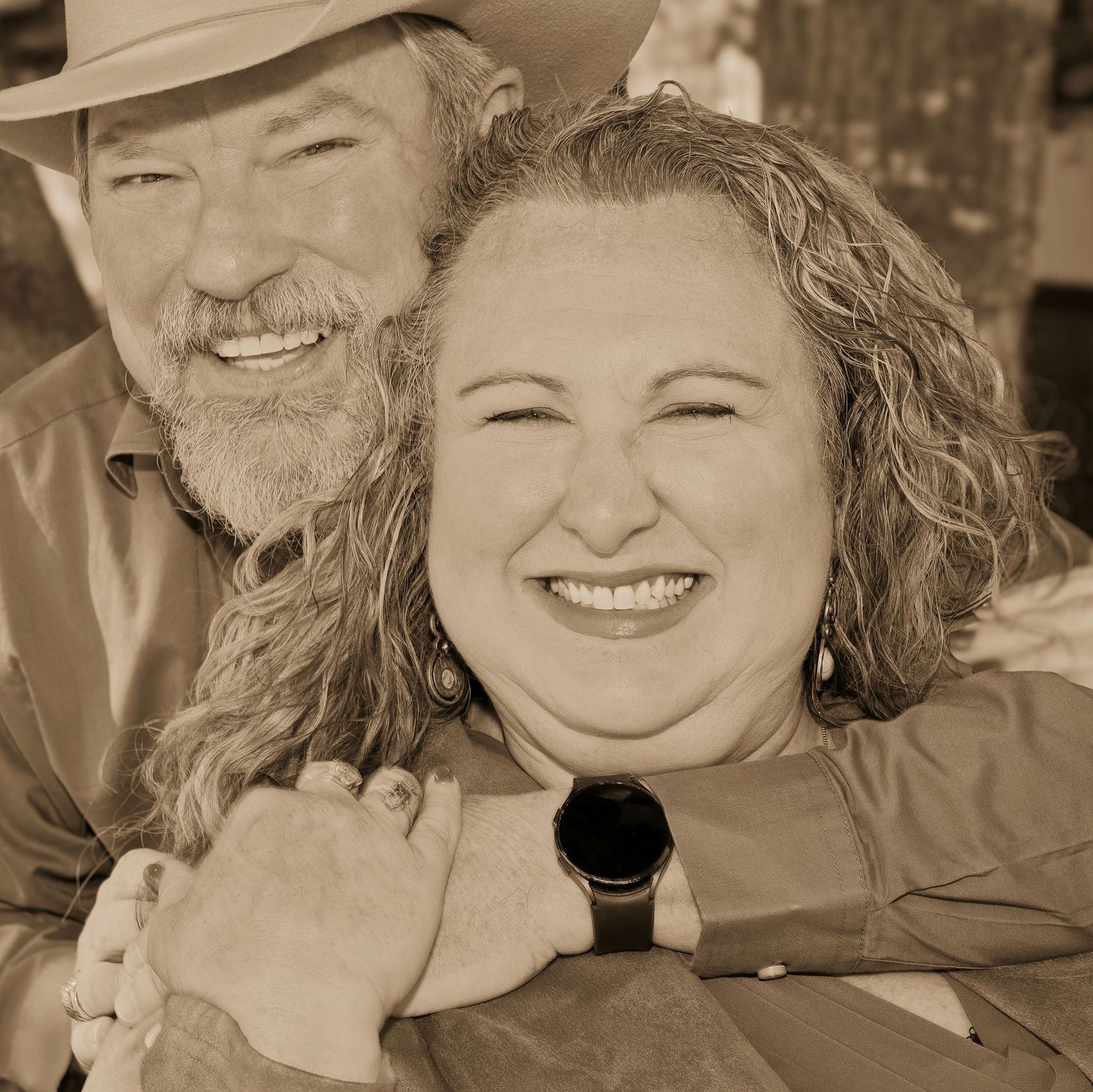 Smiling couple embracing warmly in a sepia-toned photo, man wearing cowboy hat.