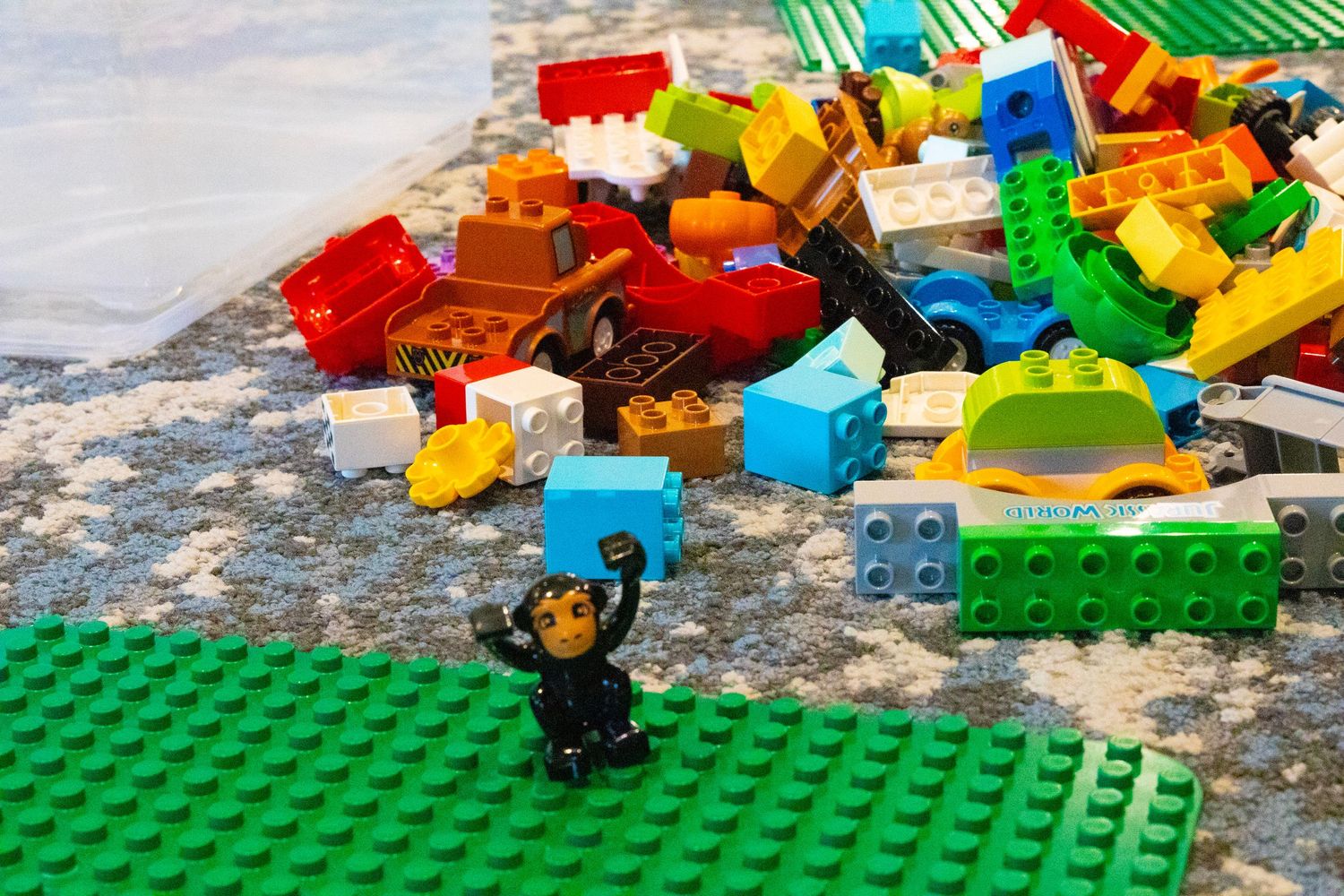 Colorful LEGO Duplo bricks scattered on a mat with a small ninja minifigure standing among the pieces.