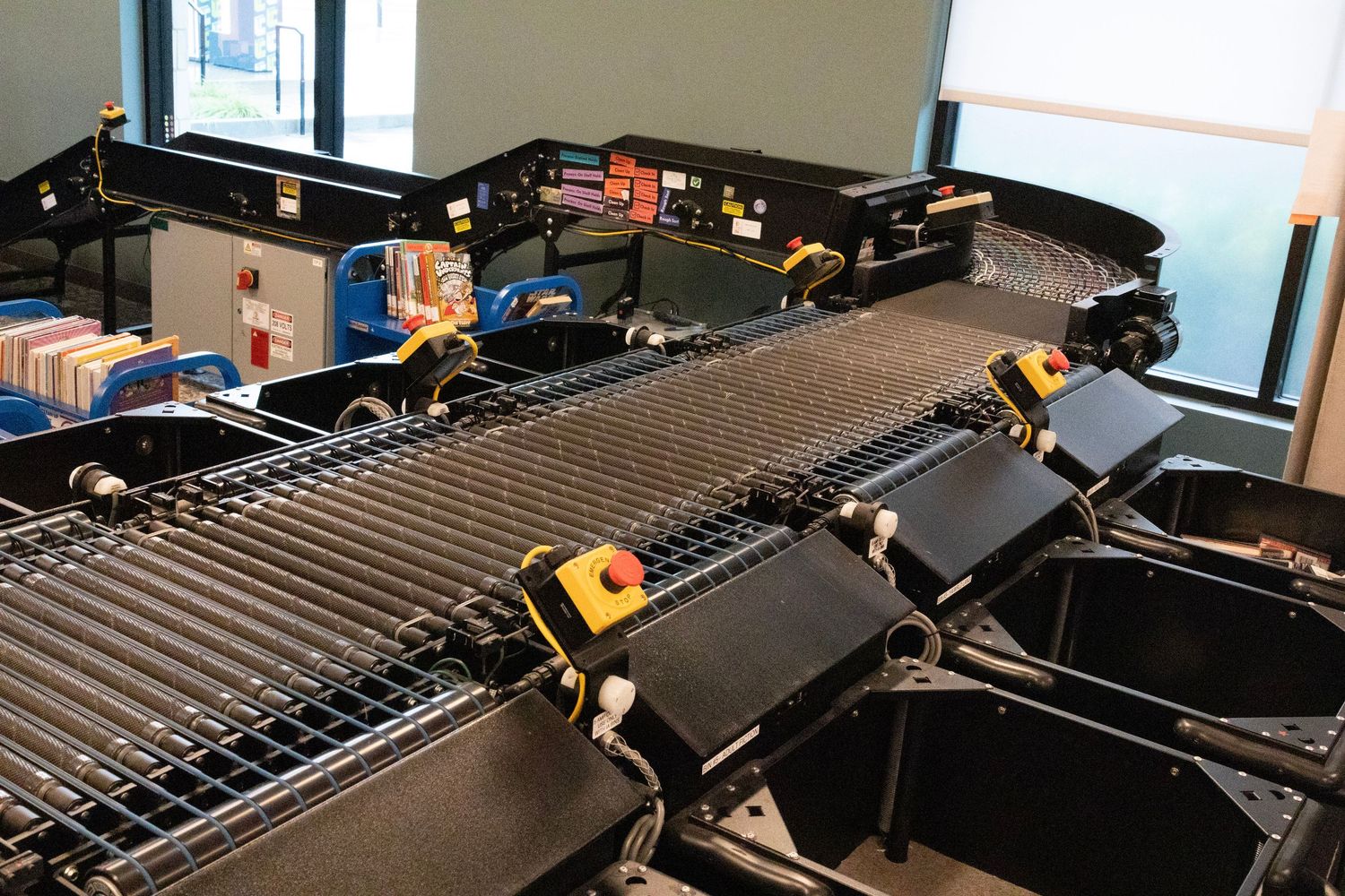Automated library book sorting conveyor belt system with RFID scanners processing returned items.