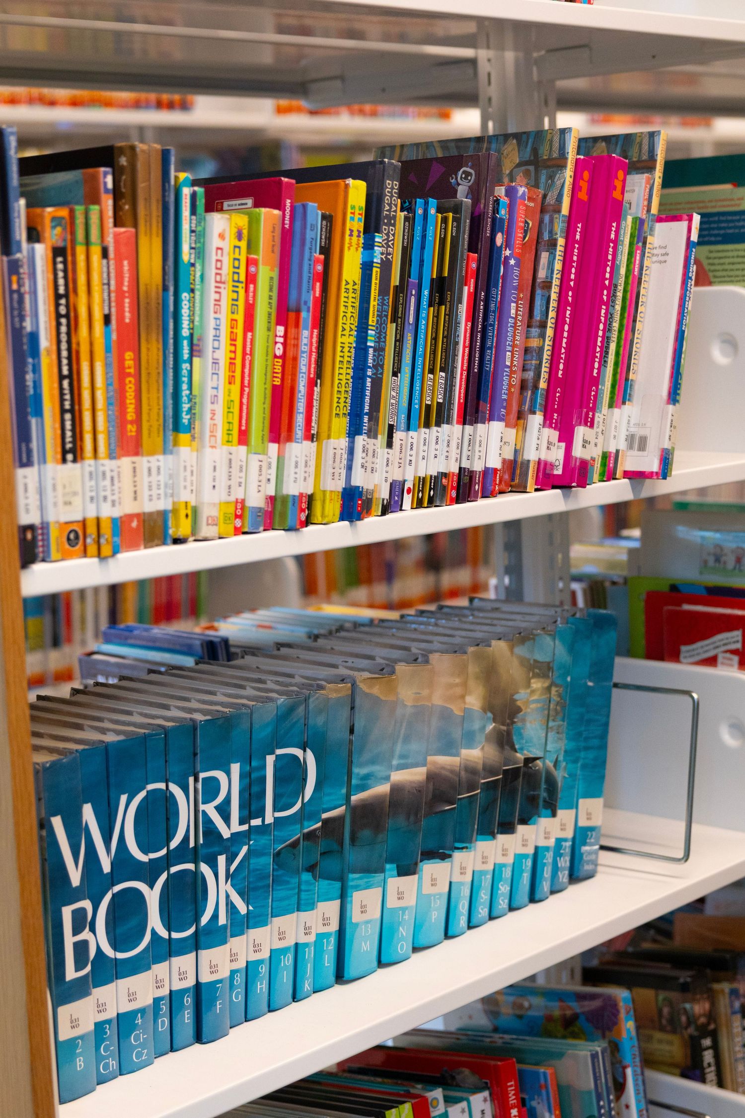 Colorful children's books and World Book encyclopedias displayed on white shelves in a library or bookstore.