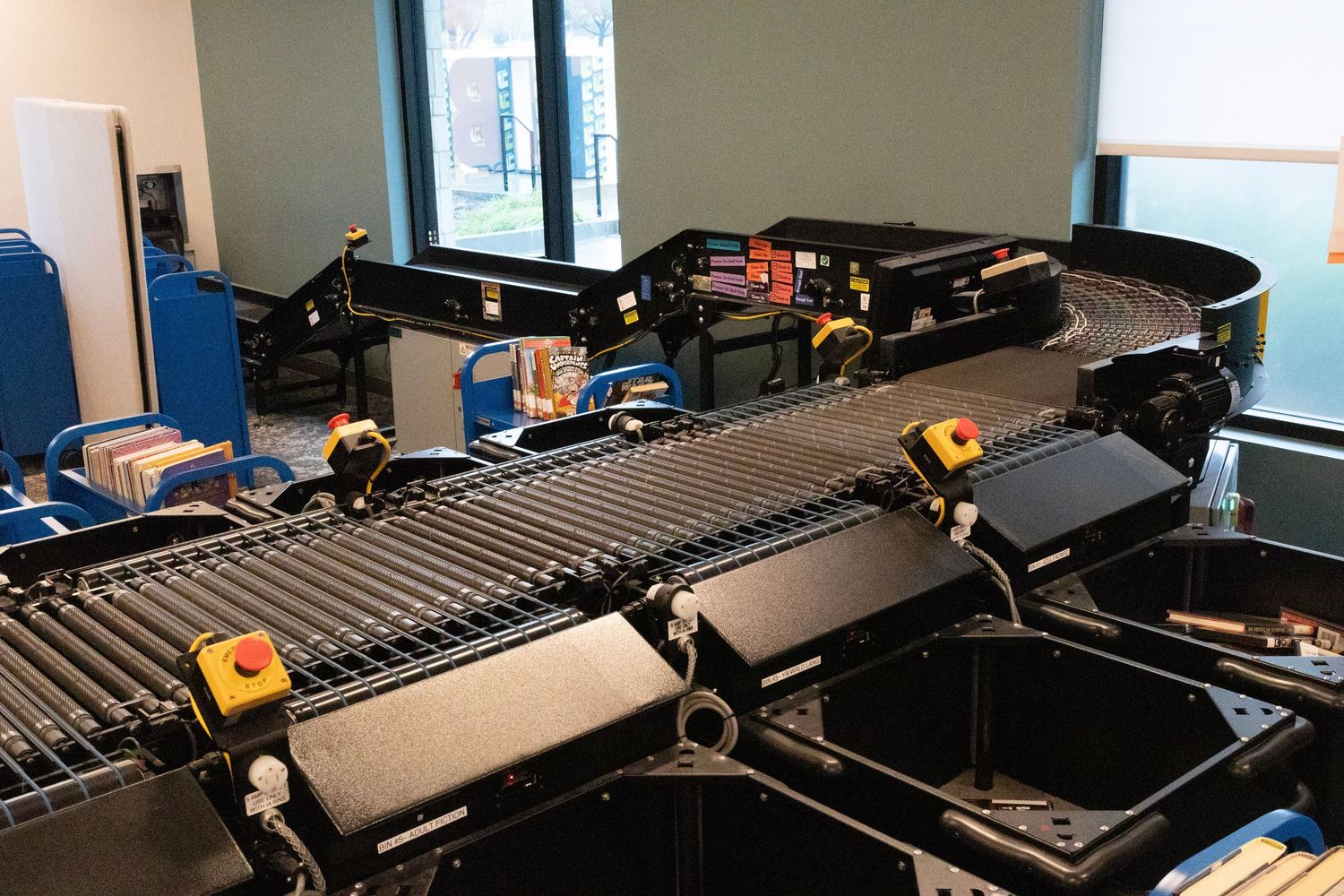 Automated library book sorting conveyor belt system with black trays in a modern facility.