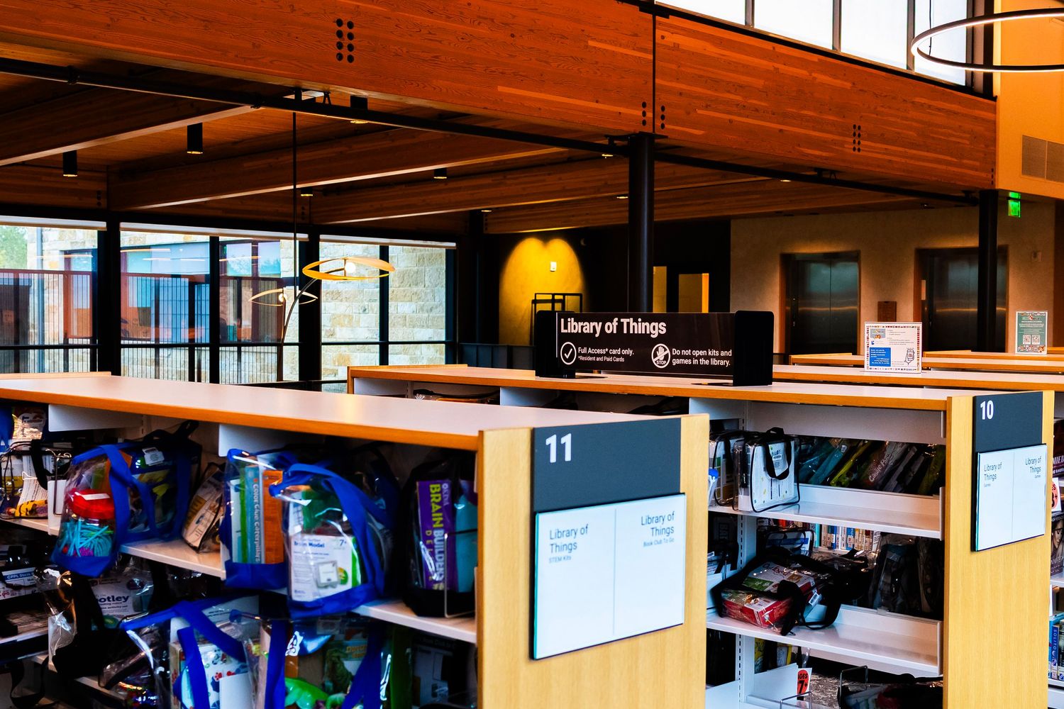 Modern library interior featuring a Library of Things display desk with shelves of items and large windows in the background.