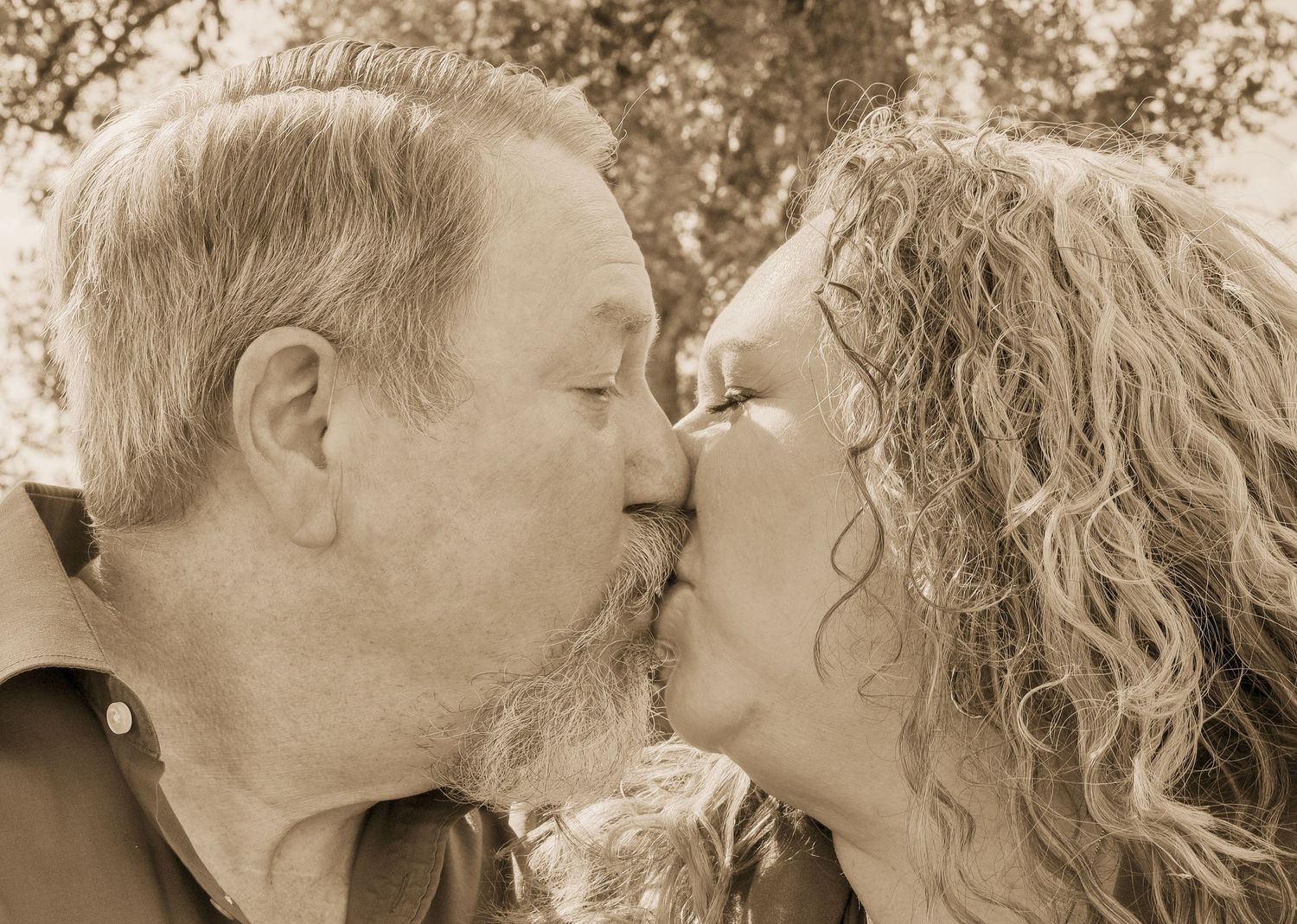 Older couple sharing a romantic kiss outdoors in a sepia-toned portrait photo.