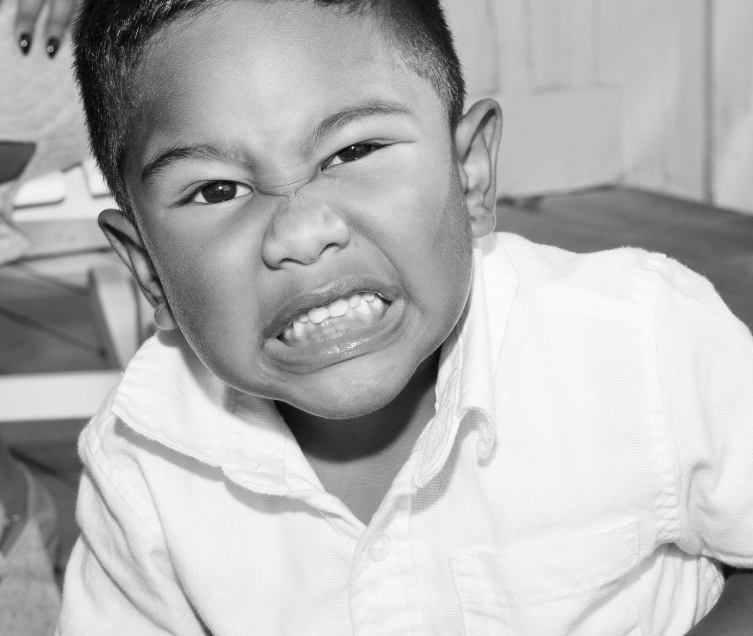 Black and white photo of a young boy in a white shirt making a fierce grimacing face showing his teeth.