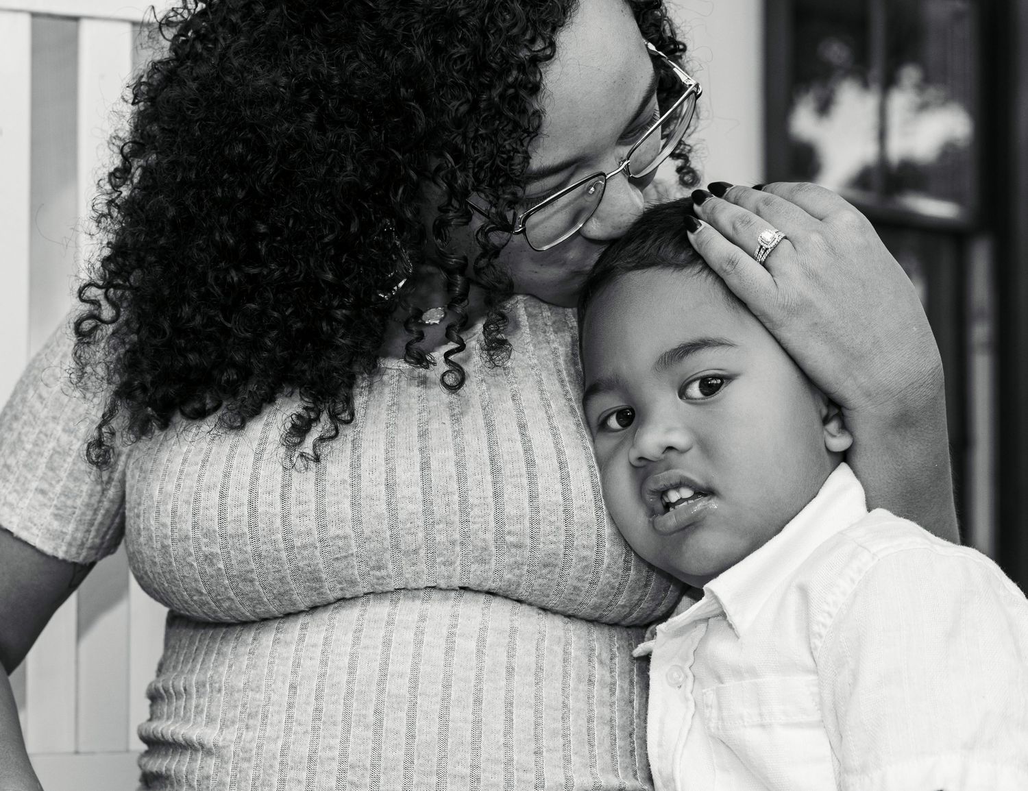 Black and white photo of a mother tenderly kissing her young son on the head while gently holding his face.