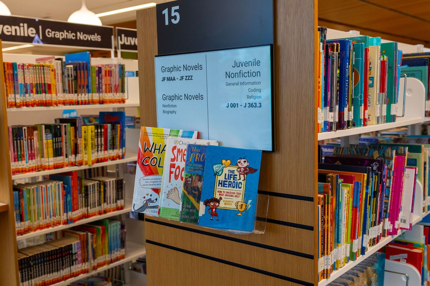 Library juvenile section signage showing Graphic Novels and Juvenile Nonfiction categories with displayed books.
