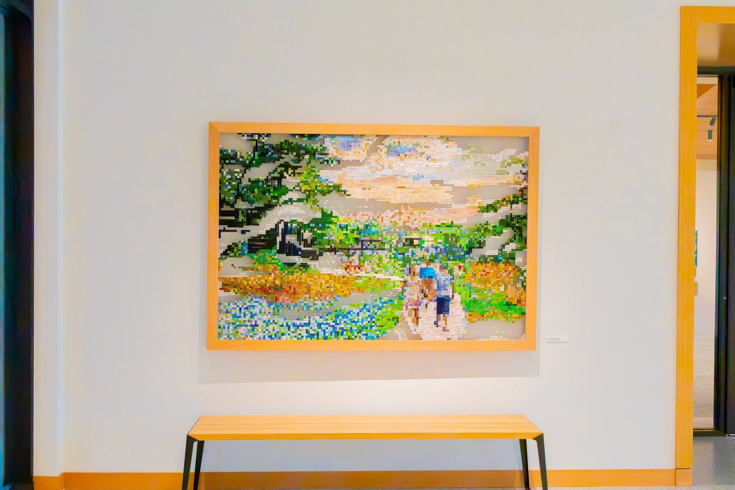 Colorful landscape painting in wooden frame showing people walking through bluebonnet fields hung on white wall.
