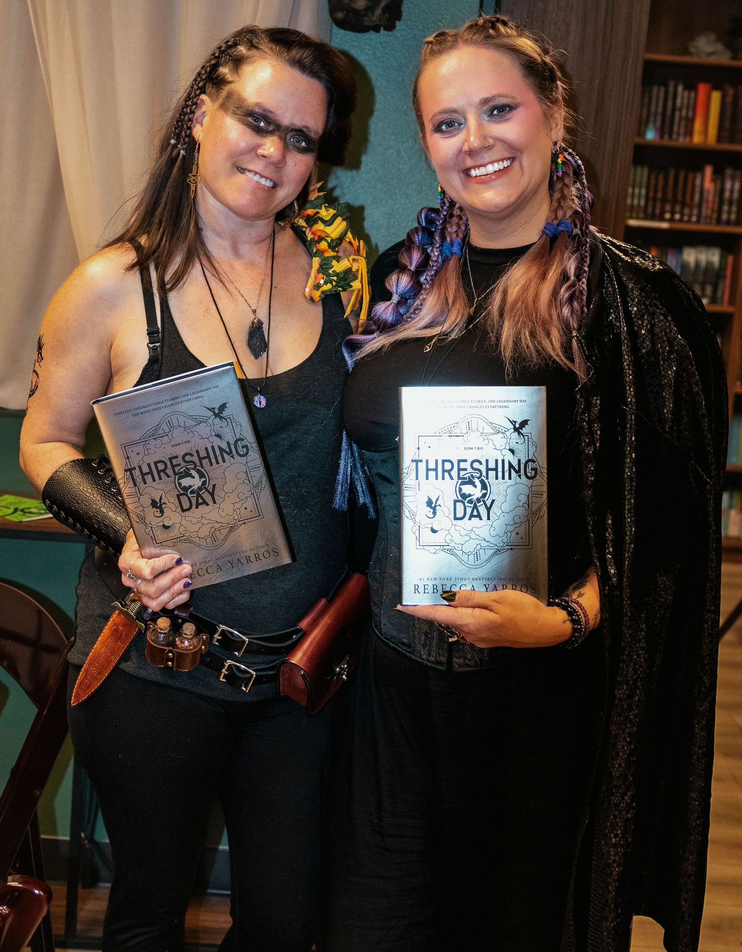 Two women in dark fantasy costumes hold copies of the book Threshing Day at a themed book launch event.