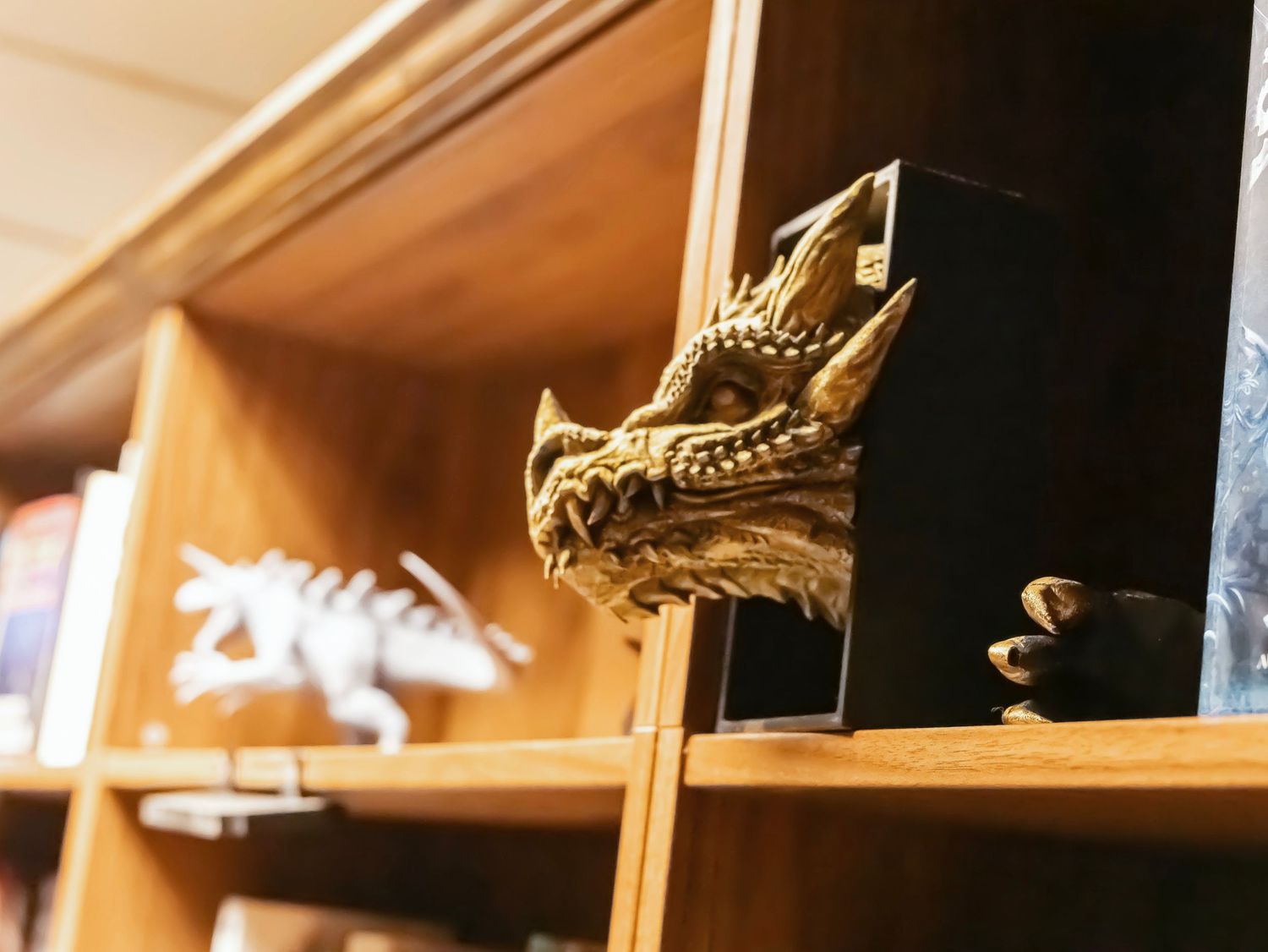 Wooden bookshelf displaying a detailed golden dragon head sculpture alongside a white dinosaur figurine.