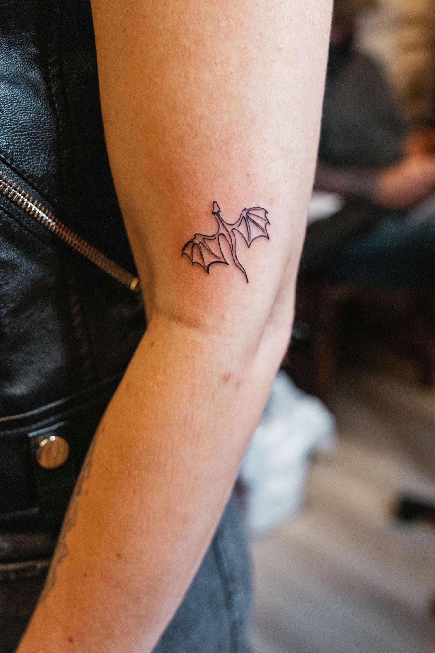 Minimalist fine line dragon tattoo on the inner arm, done in black ink outline style.