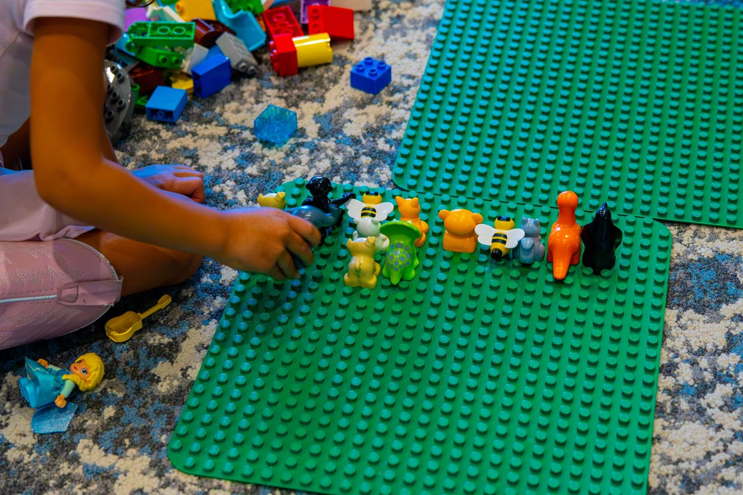 Young child playing with colorful LEGO figures and blocks on green base plates.