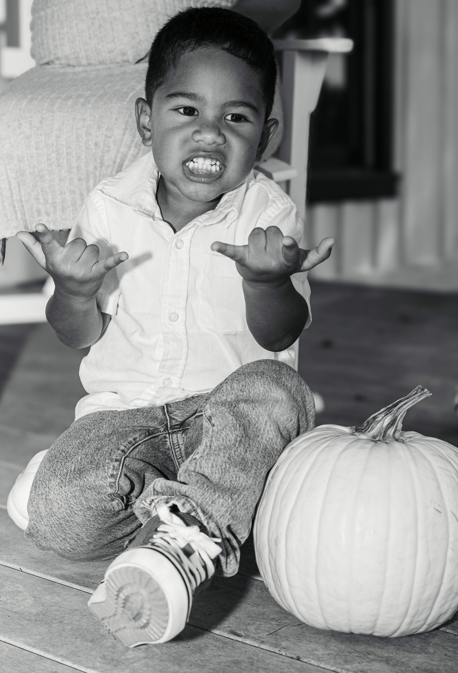 Black and white photo of a toddler boy making a scary face next to a pumpkin, perfect for Halloween.