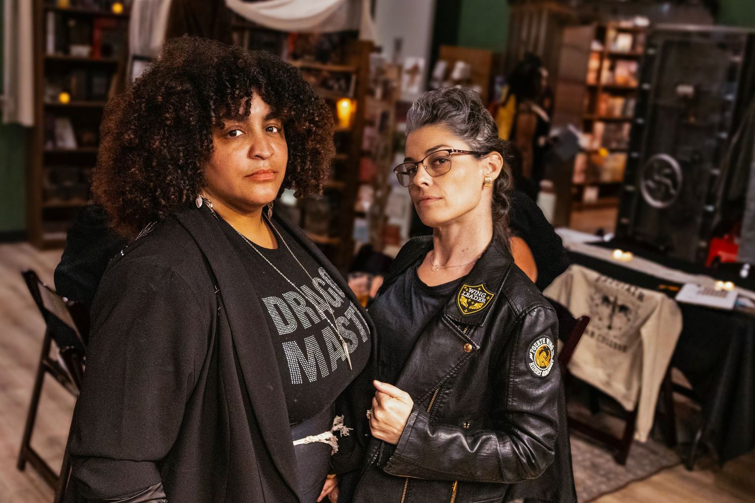 Two women posing together at an indoor event, one wearing a Dungeon Master shirt and the other in a leather jacket.