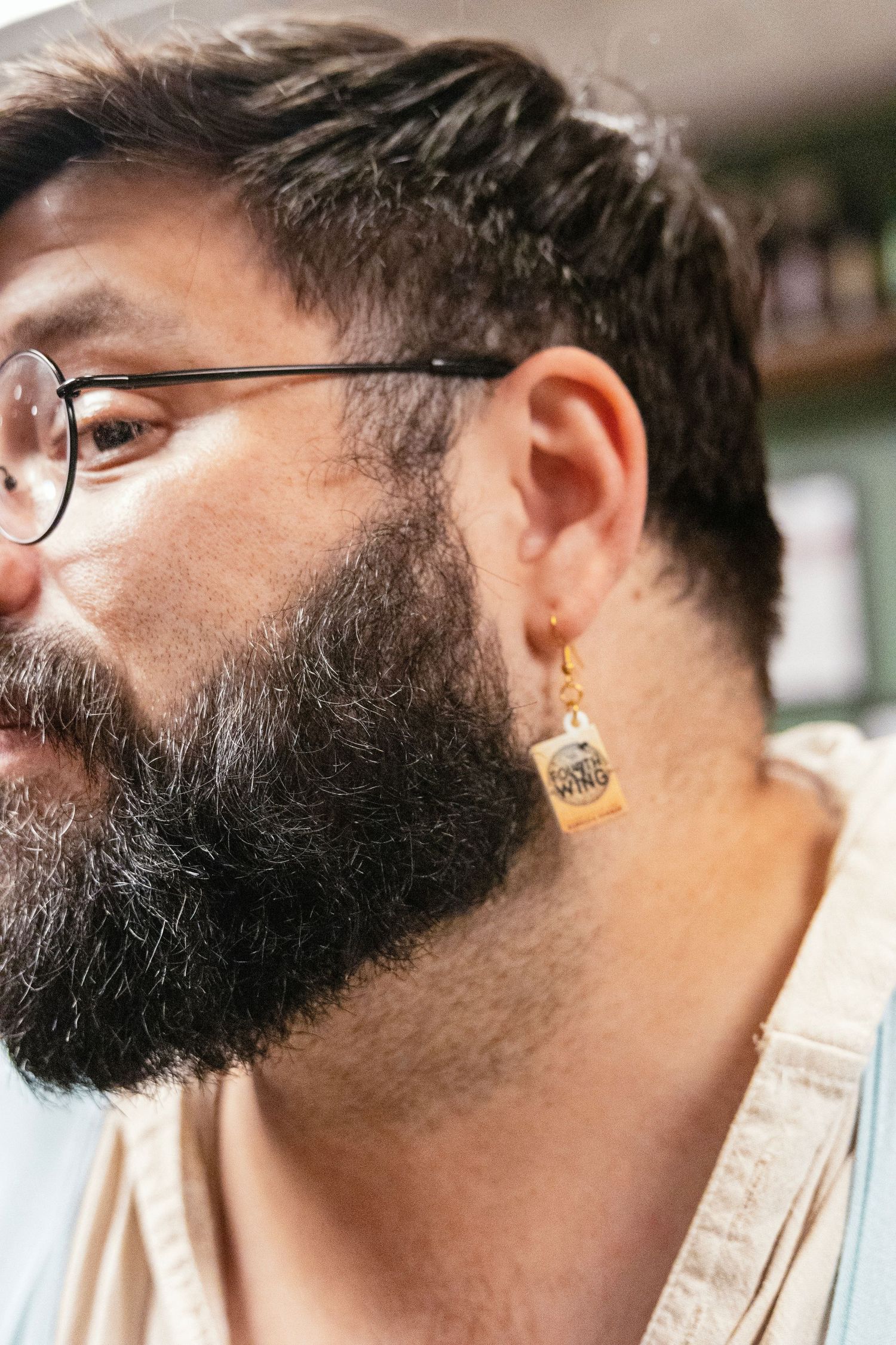 Bearded man with glasses wearing a miniature whiskey bottle earring as a unique accessory.
