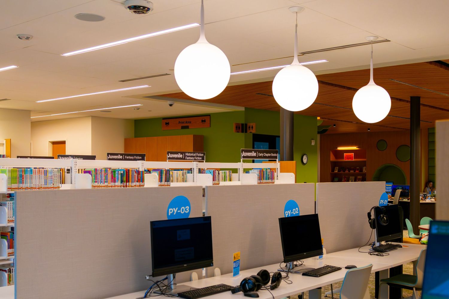 Modern library computer workstations with globe pendant lights and colorful bookshelves.