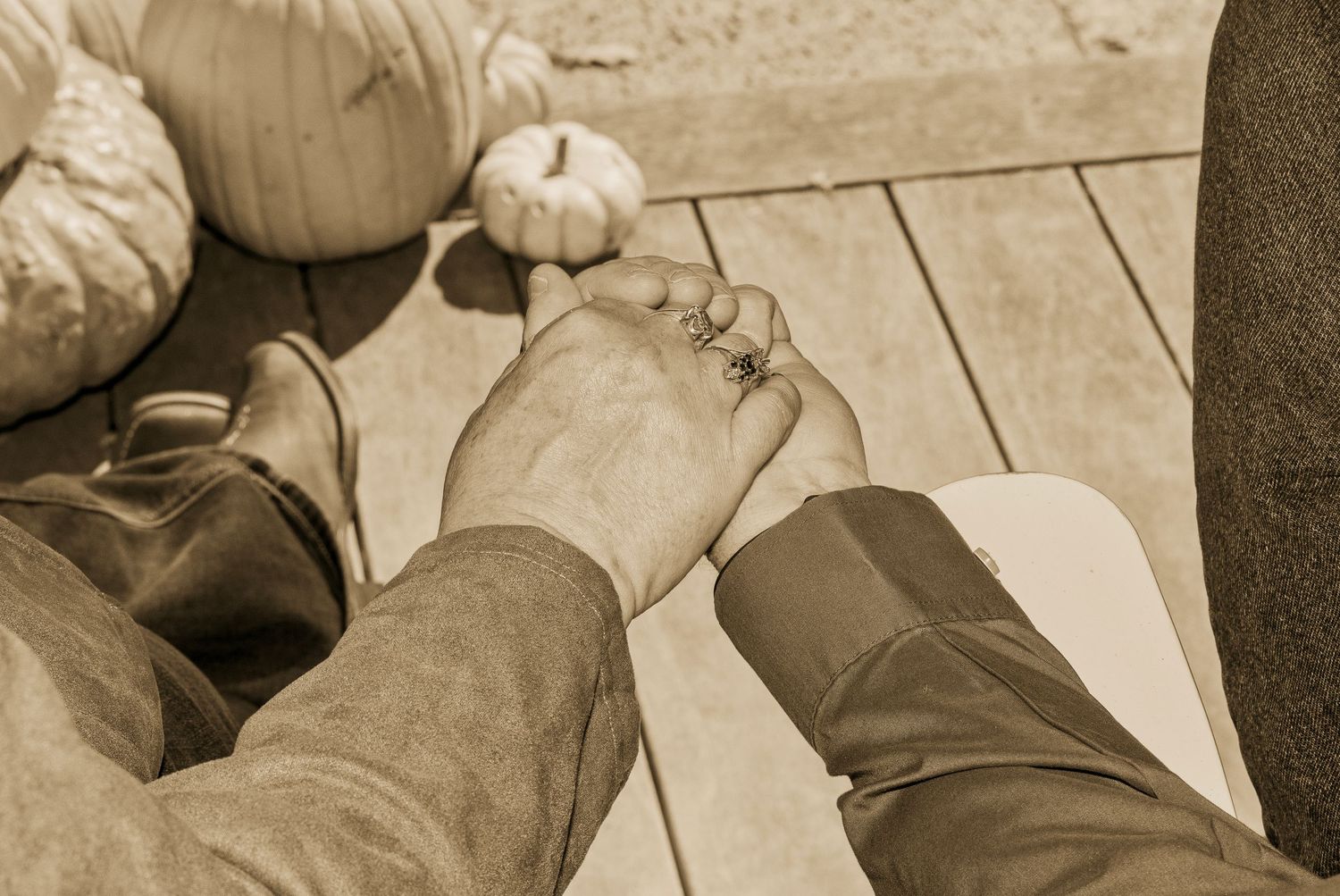 Couple holding hands tenderly outdoors near pumpkins, sepia-toned romantic photo capturing love and togetherness.