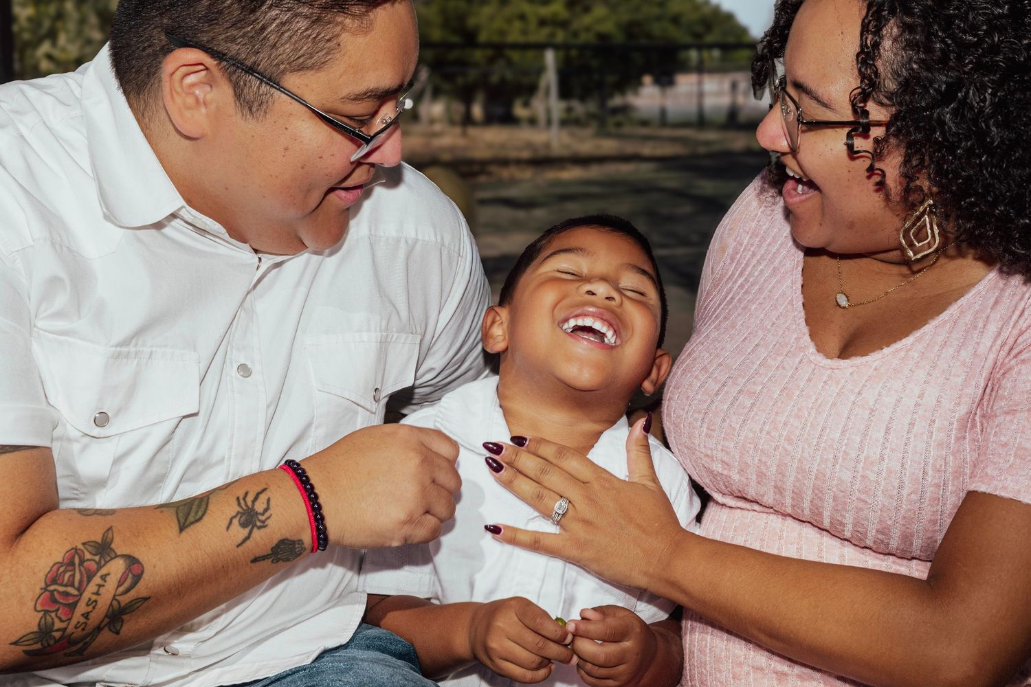 A joyful family of three laughing together outdoors, with parents sharing a fun moment with their young son.