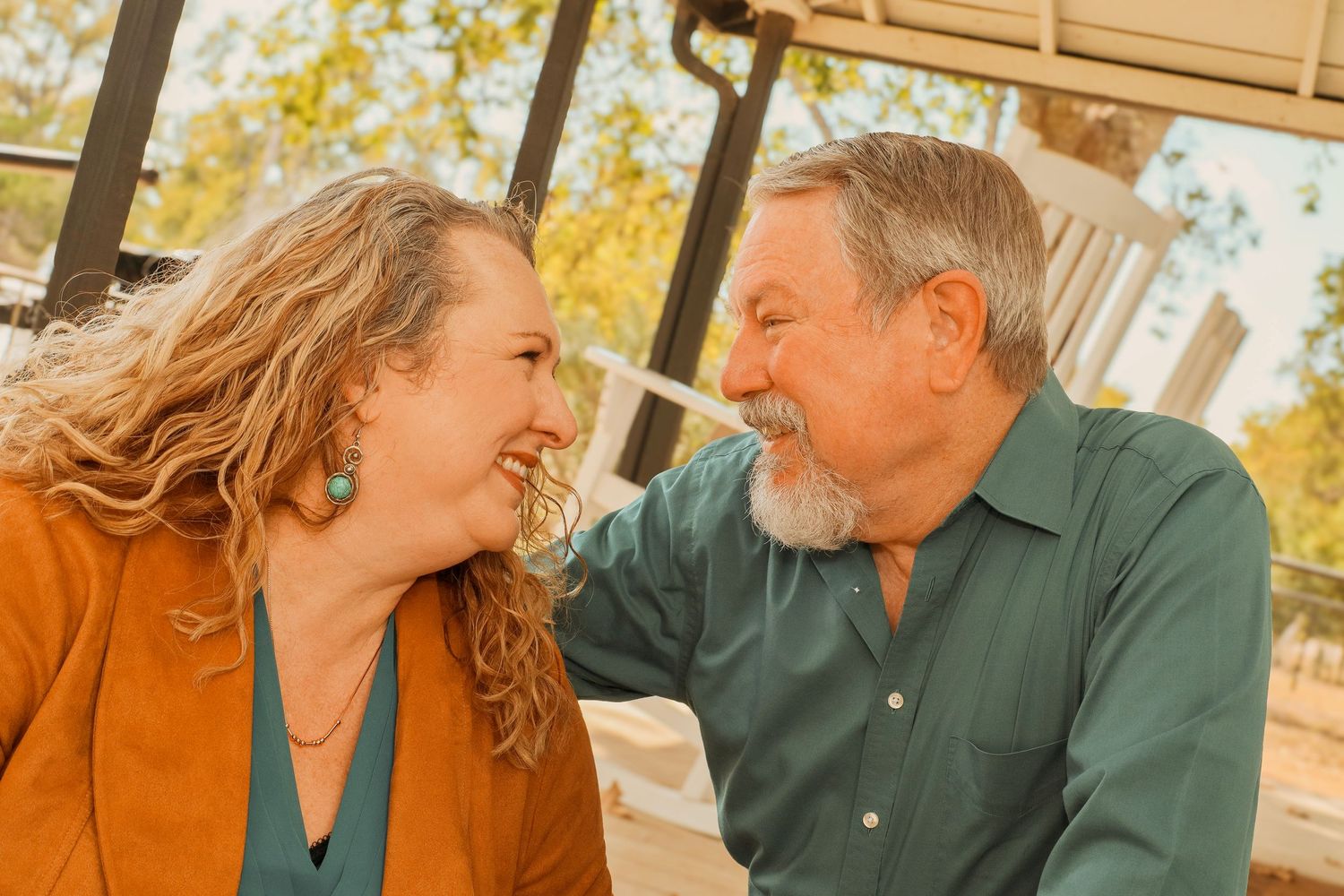 A smiling man and woman share a joyful moment outdoors, surrounded by autumn foliage.