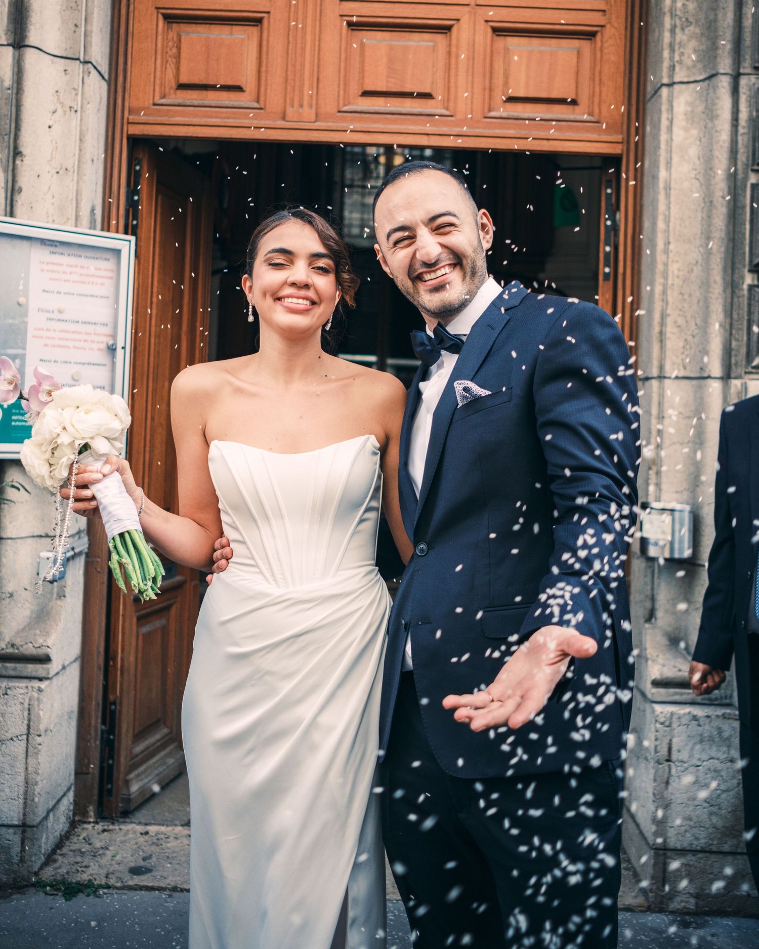 A joyful newlywed couple celebrates outside a church door, showered with confetti, bride holding a bouquet.