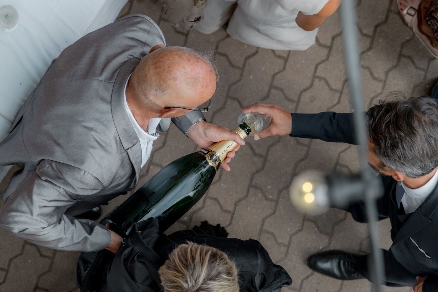 Aerial view of man opening champagne bottle at celebration event on brick patio.